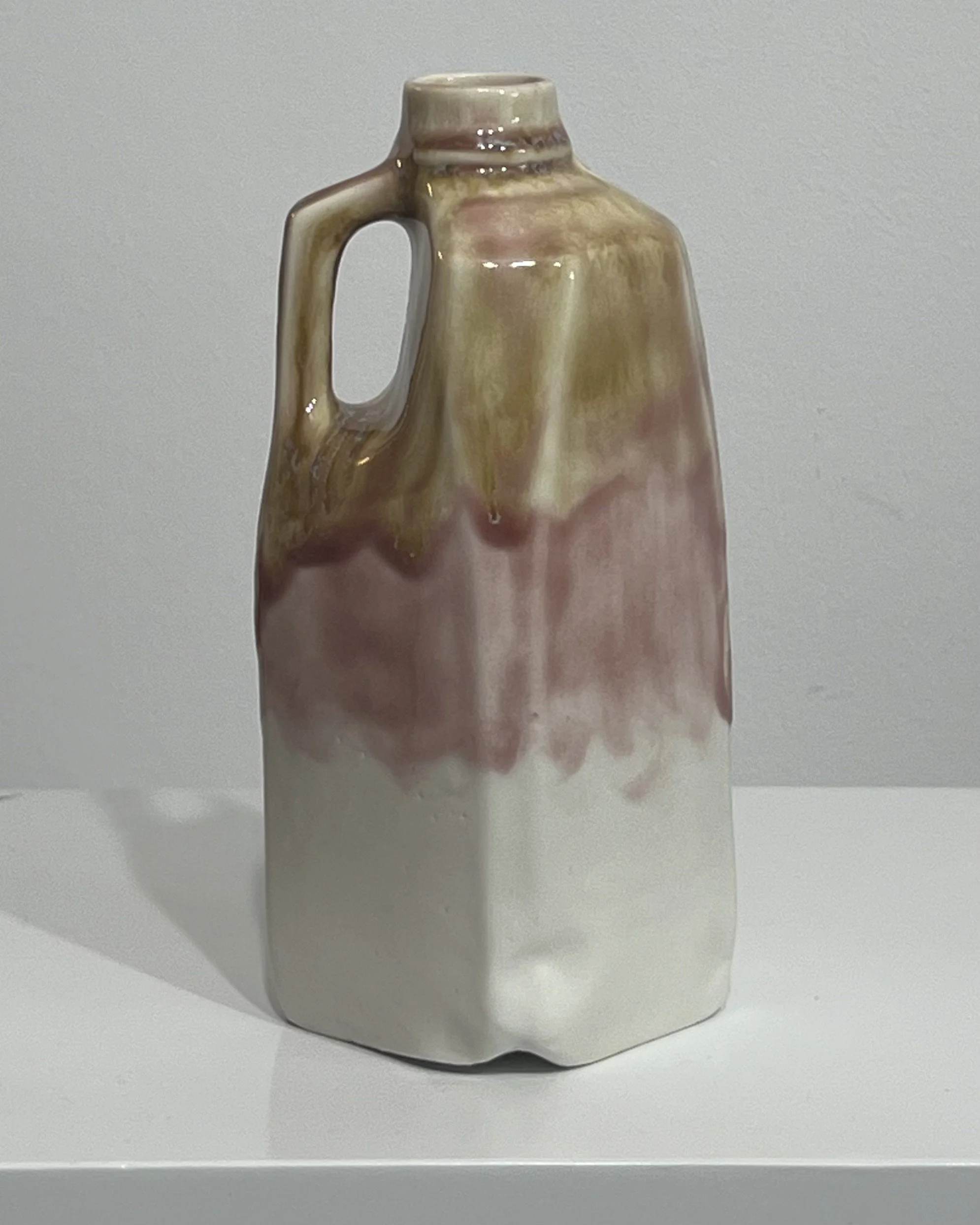 Side view of tall handmade milk jug vase showing irregular sculptural form and layered green, mauve, and cream glaze.