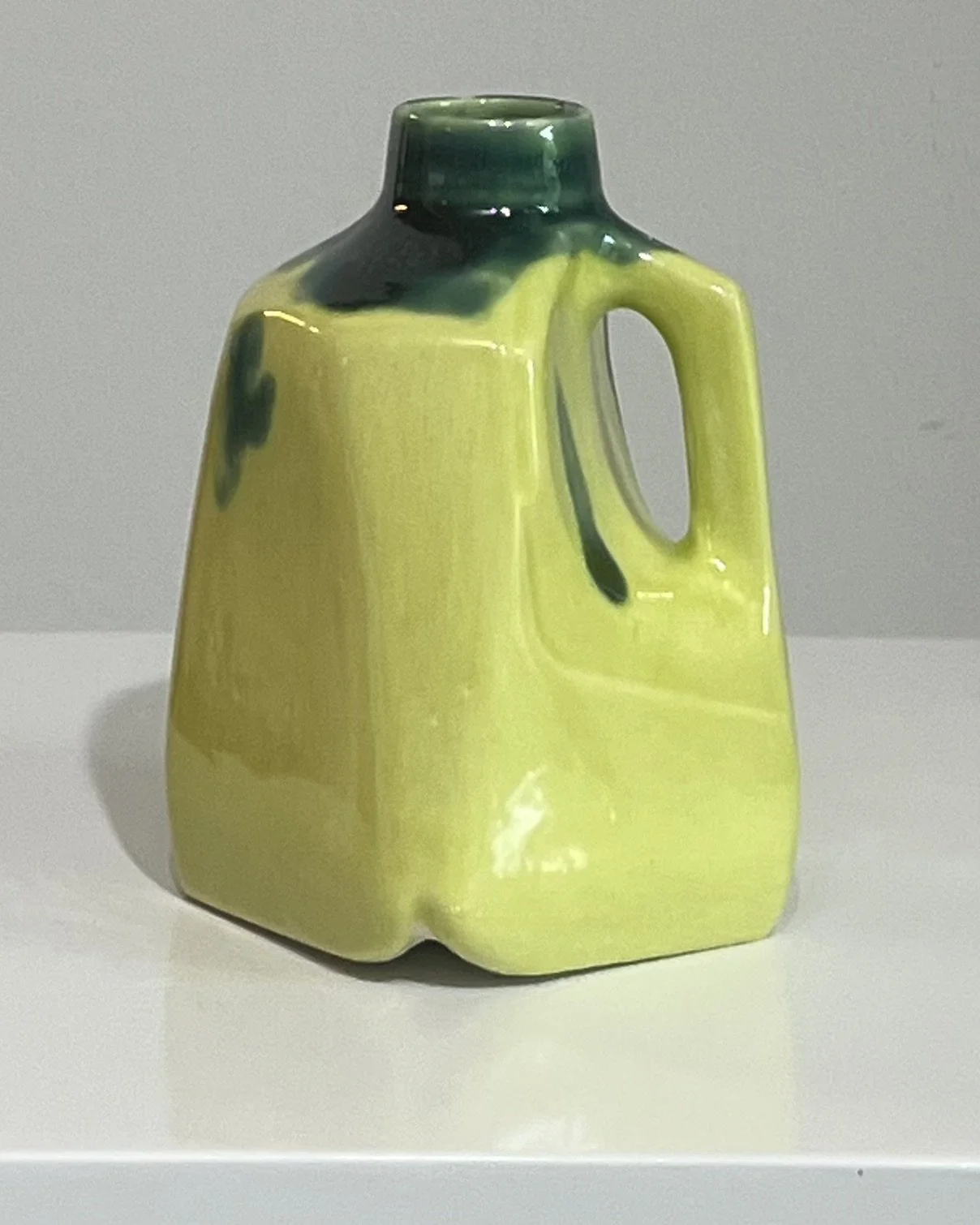 Front angled view of a handmade porcelain milk jug with vibrant lime green and dark green glazes.