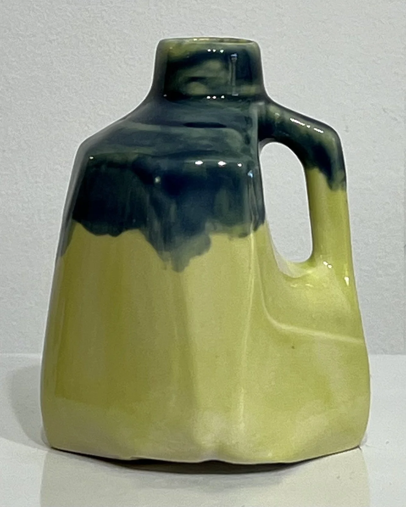 Front view of a handmade porcelain milk jug with dark blue glaze flowing over bright yellow-green ceramic