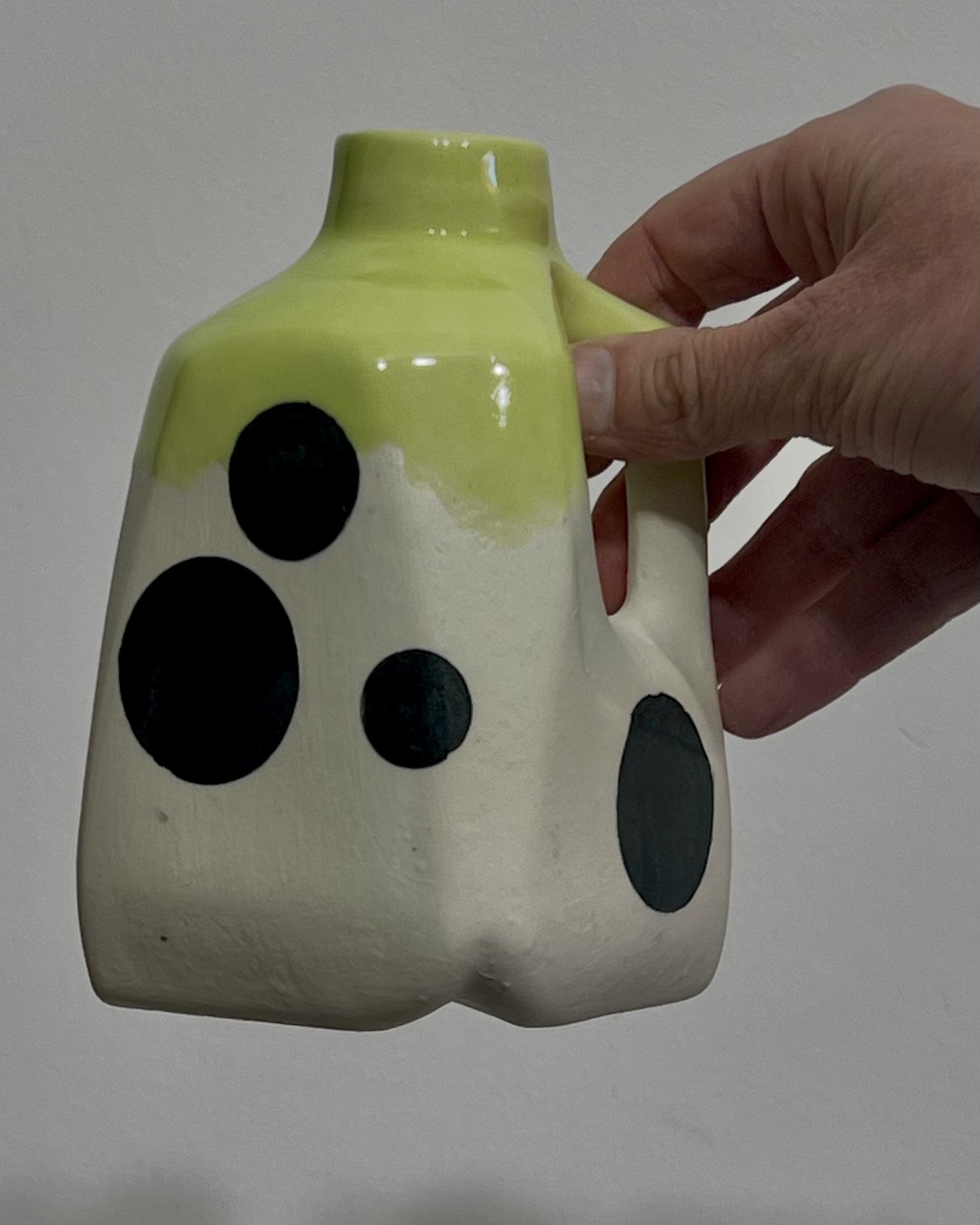 Hand holding black polka dot porcelain milk jug No. 26.150 by Alissa Van Atta, demonstrating the ceramic vessel's small size and squared silhouette.