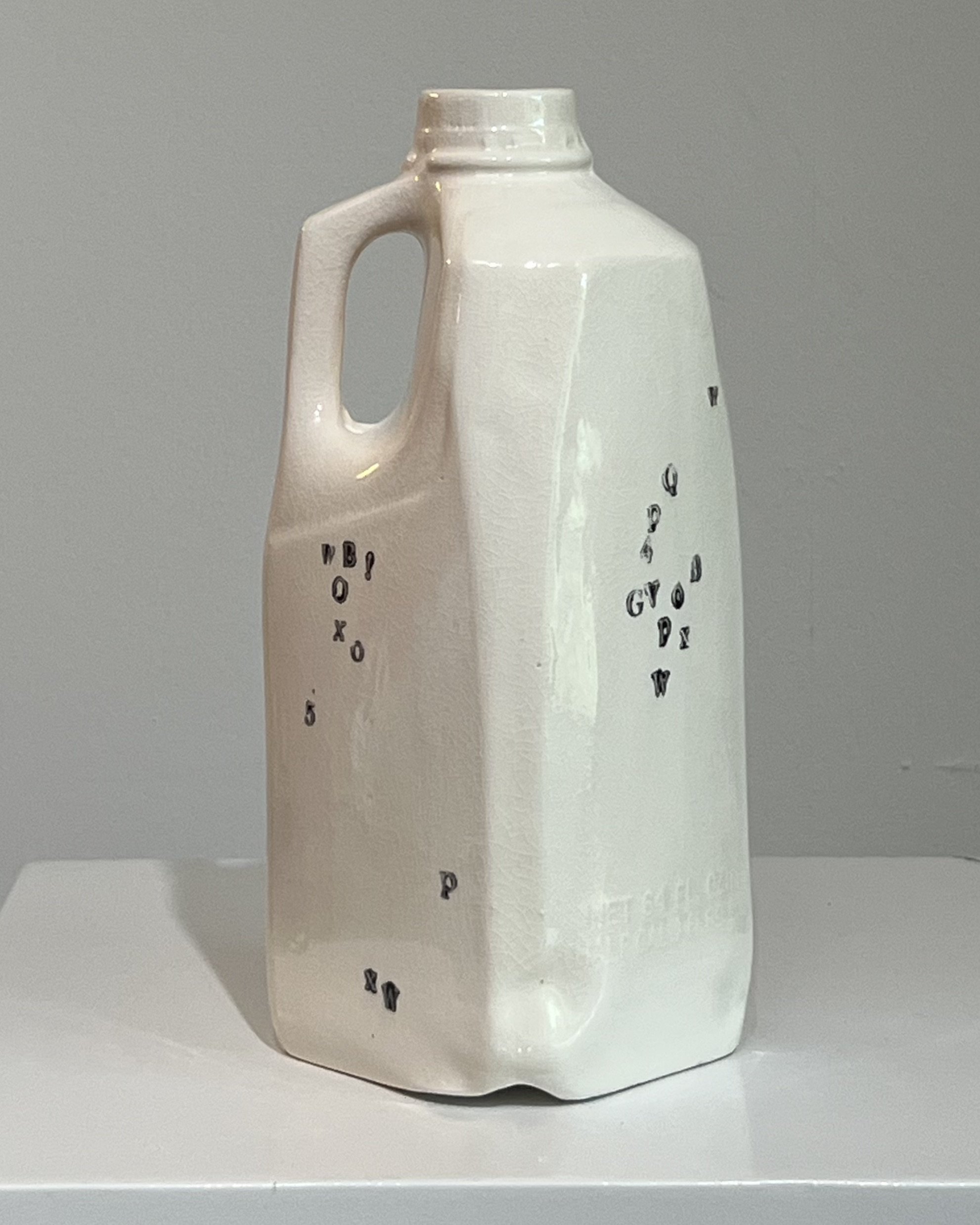 Rear view of a handbuilt tall porcelain milk jug showing sculptural form and fragmented black typography.