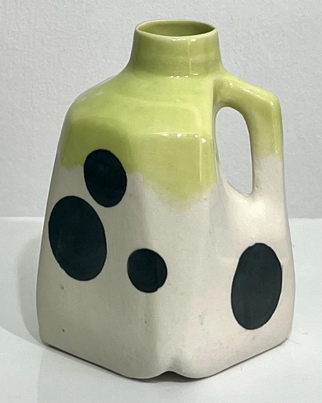 Front view of handmade porcelain milk jug No. 26.150 by Alissa Van Atta, featuring oversized black polka dots on a cream body with bright yellow-green Pear glaze.