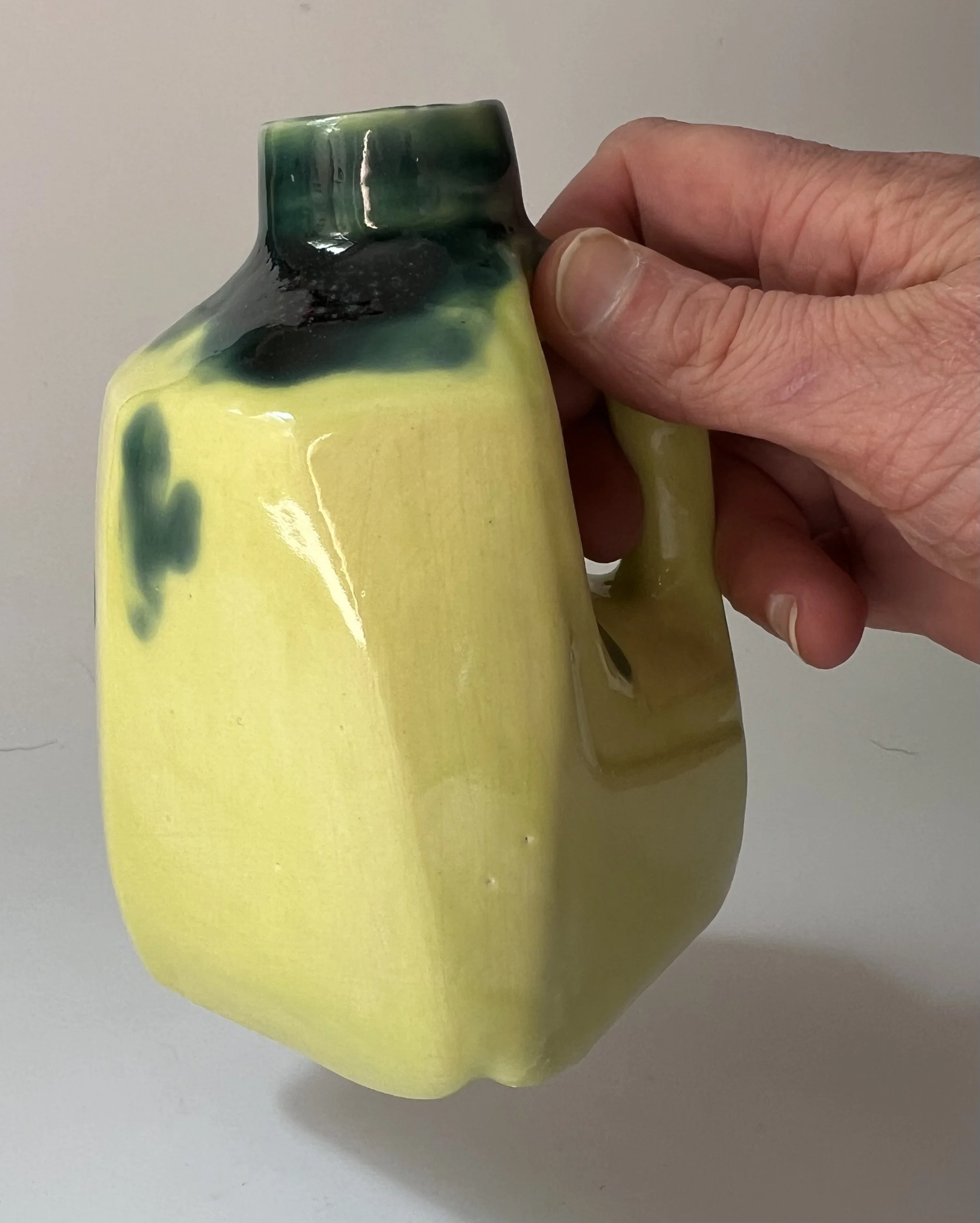 Hand holding a handmade porcelain milk jug to show its scale and sculptural form.