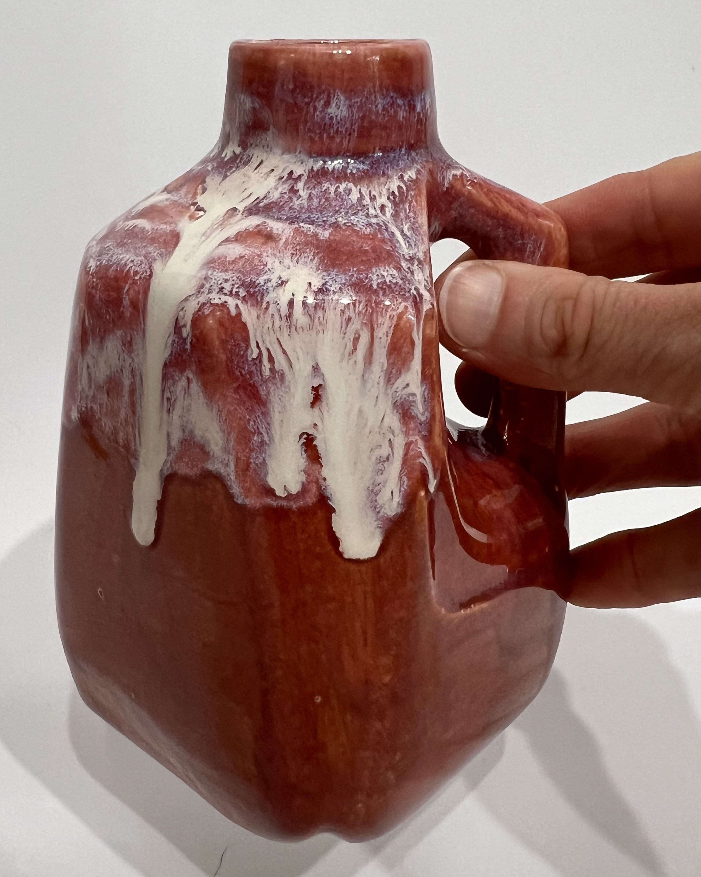Handmade red porcelain milk jug held in hand to demonstrate its compact size