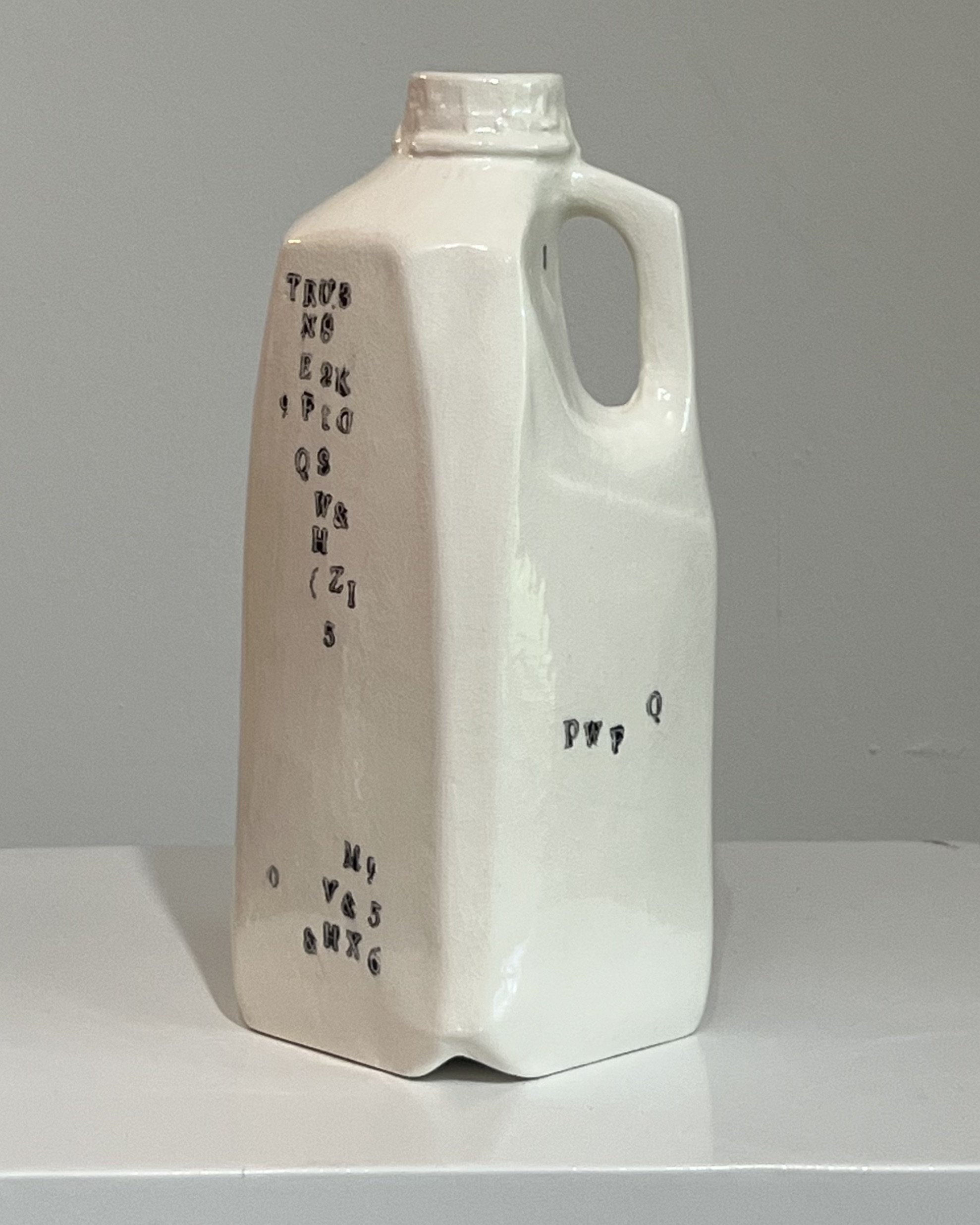 Front view of a tall handbuilt white porcelain milk jug with scattered black typographic impressions.