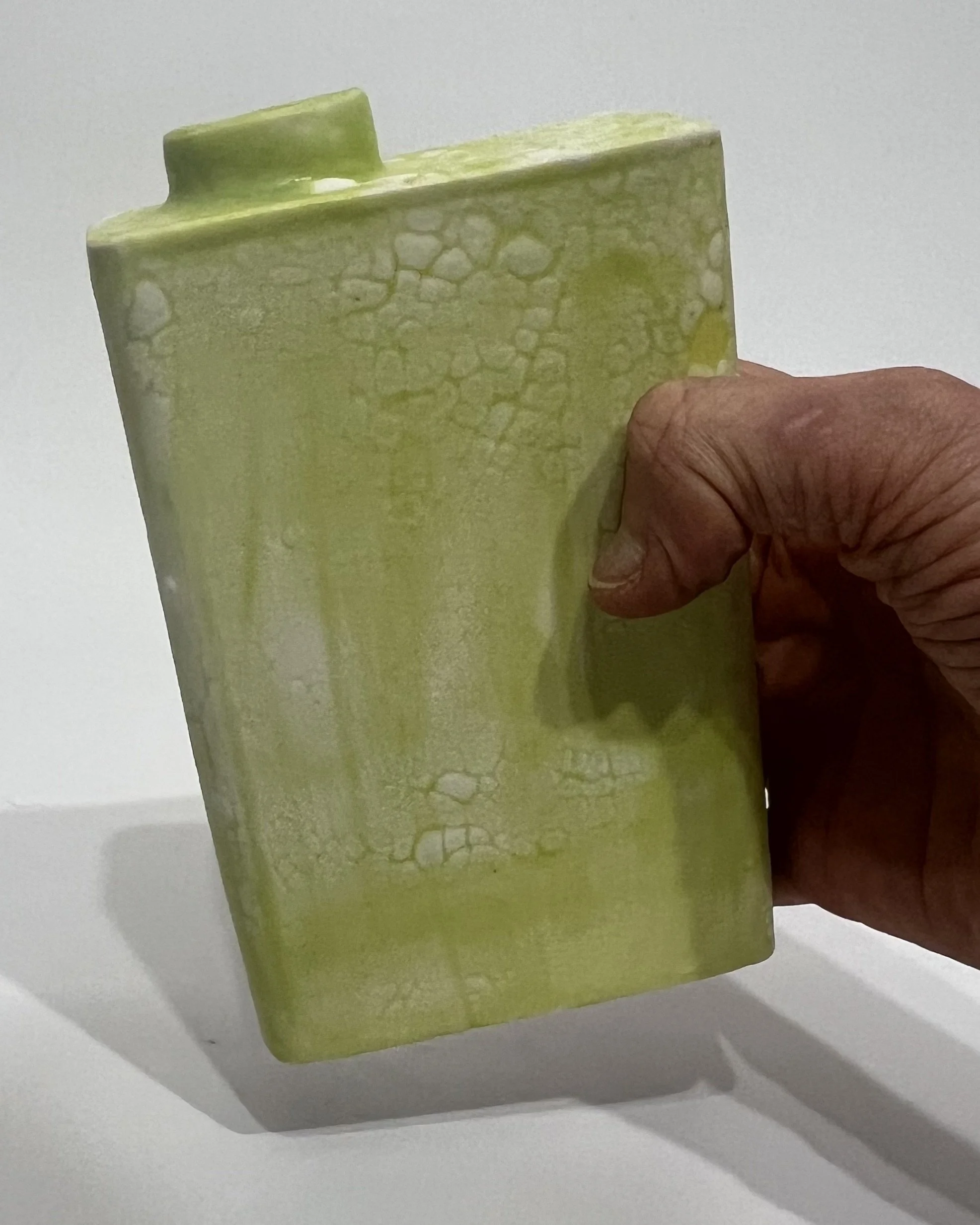 Hand holding a small handmade chartreuse porcelain Carton vessel to show its size and proportions.
