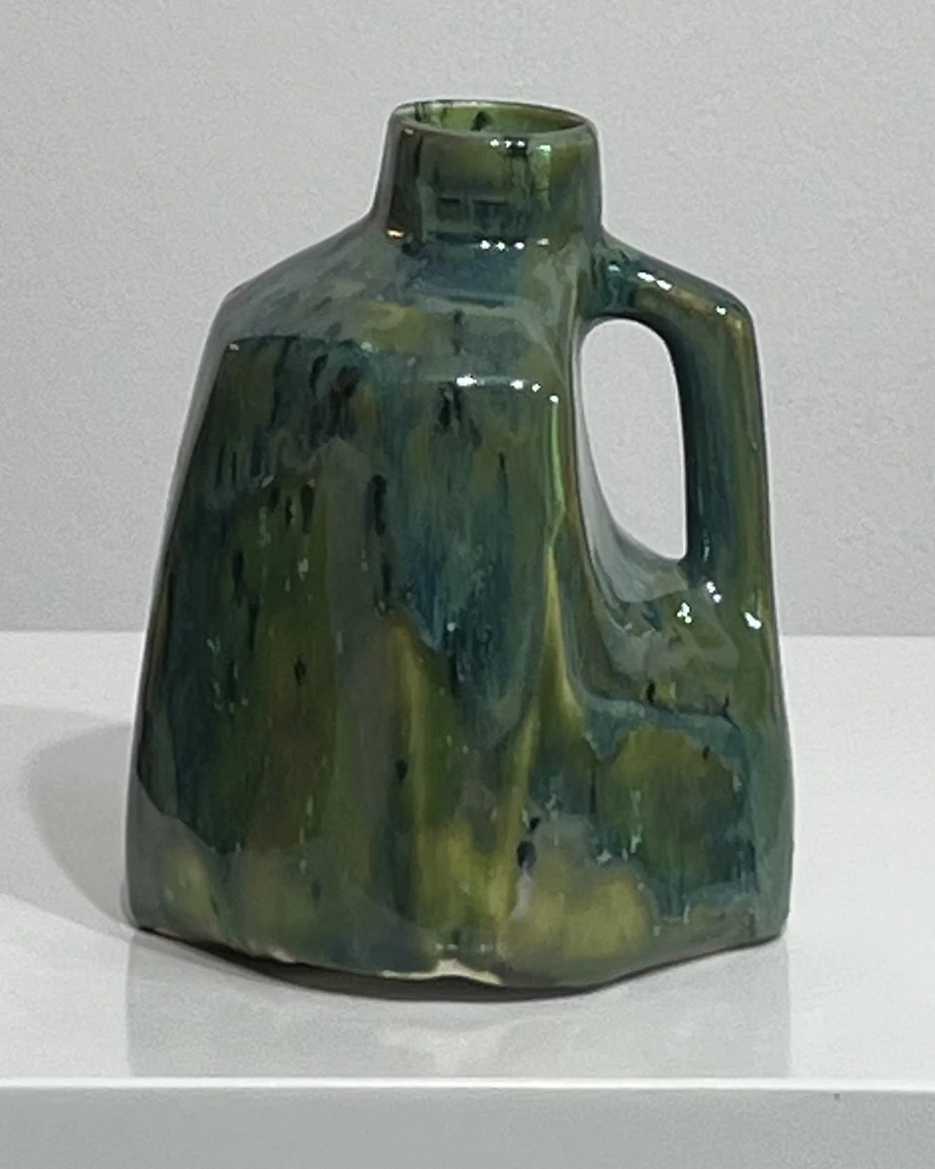 Front view of handmade porcelain milk jug with flowing Lime Shower and Seaweed glazes in deep green and turquoise.