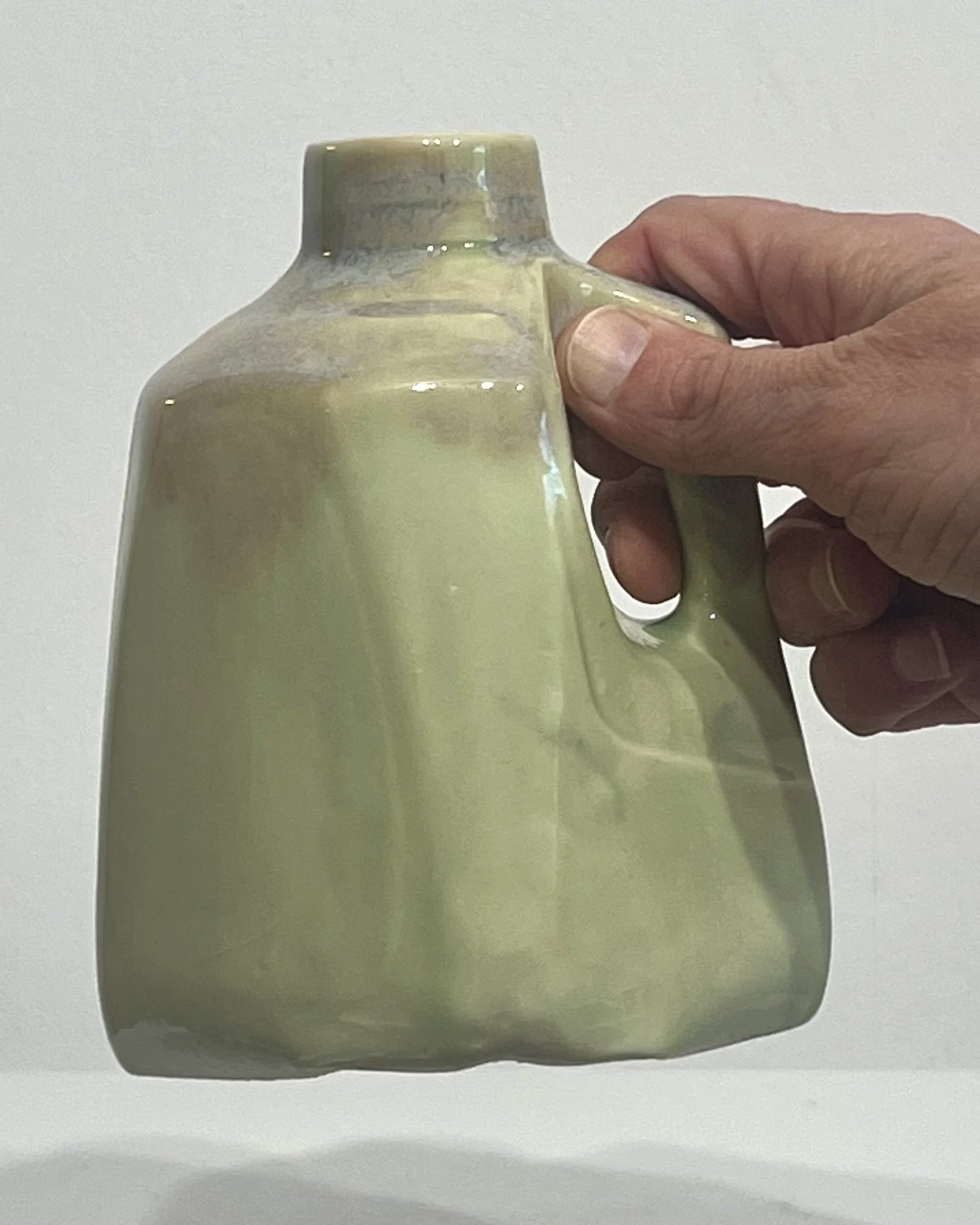 Hand holding a small pale-green porcelain milk jug by Alissa Van Atta to demonstrate its scale.