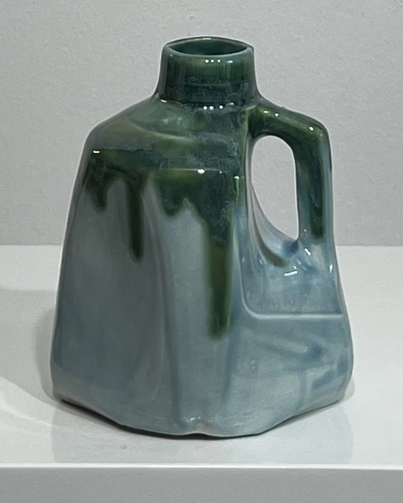 Front view of a handbuilt ceramic milk jug vessel with soft blue-green glaze and glossy dark green drips.