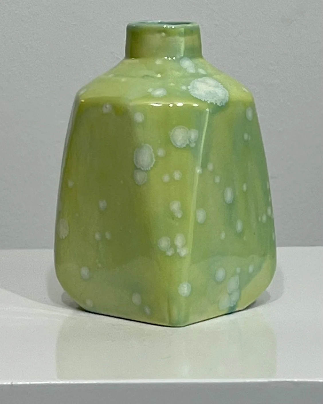 Angled view of handmade porcelain milk jug featuring layered green glazes and crystalline celadon effects.
