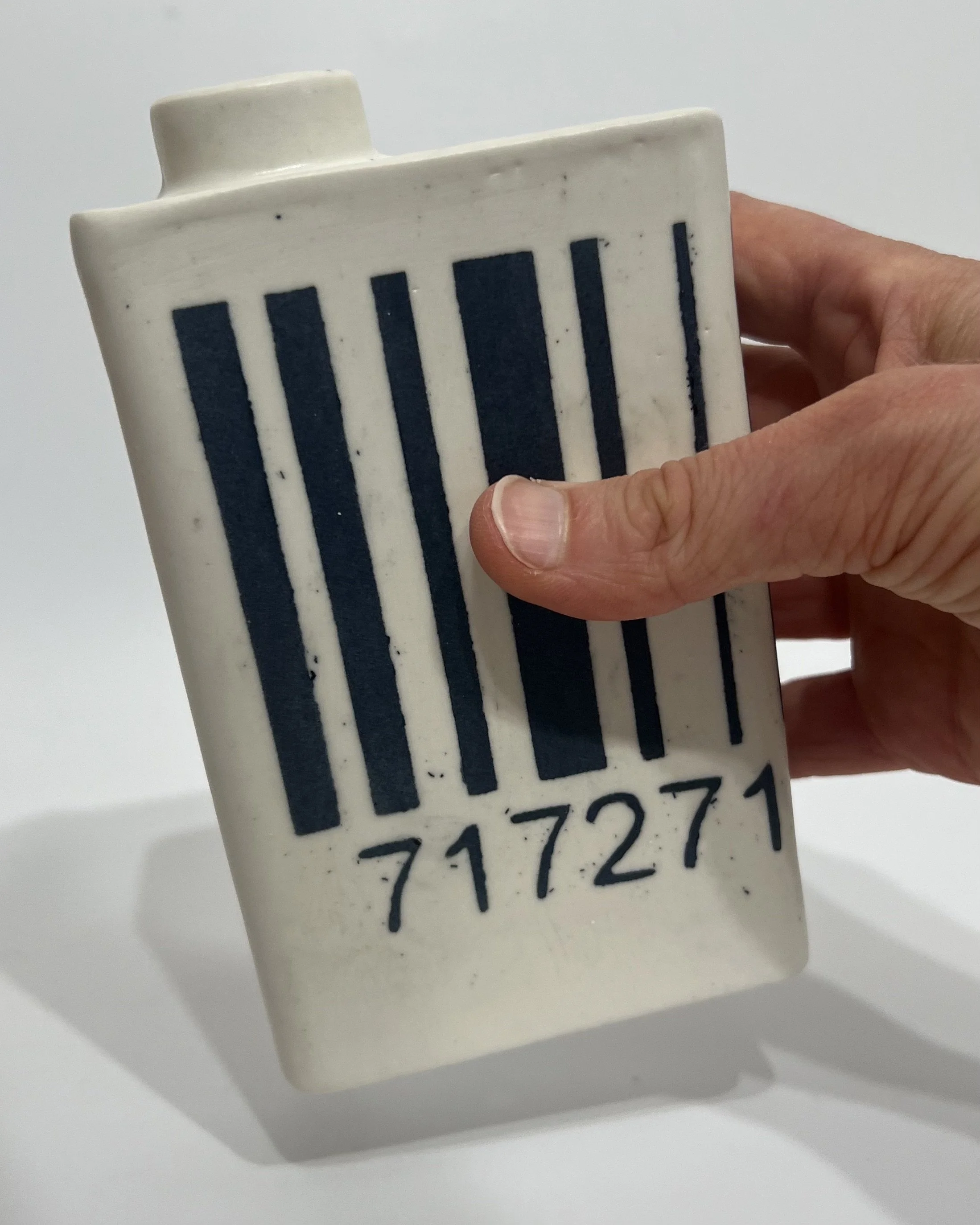 Hand holding small porcelain barcode milk carton to show scale
