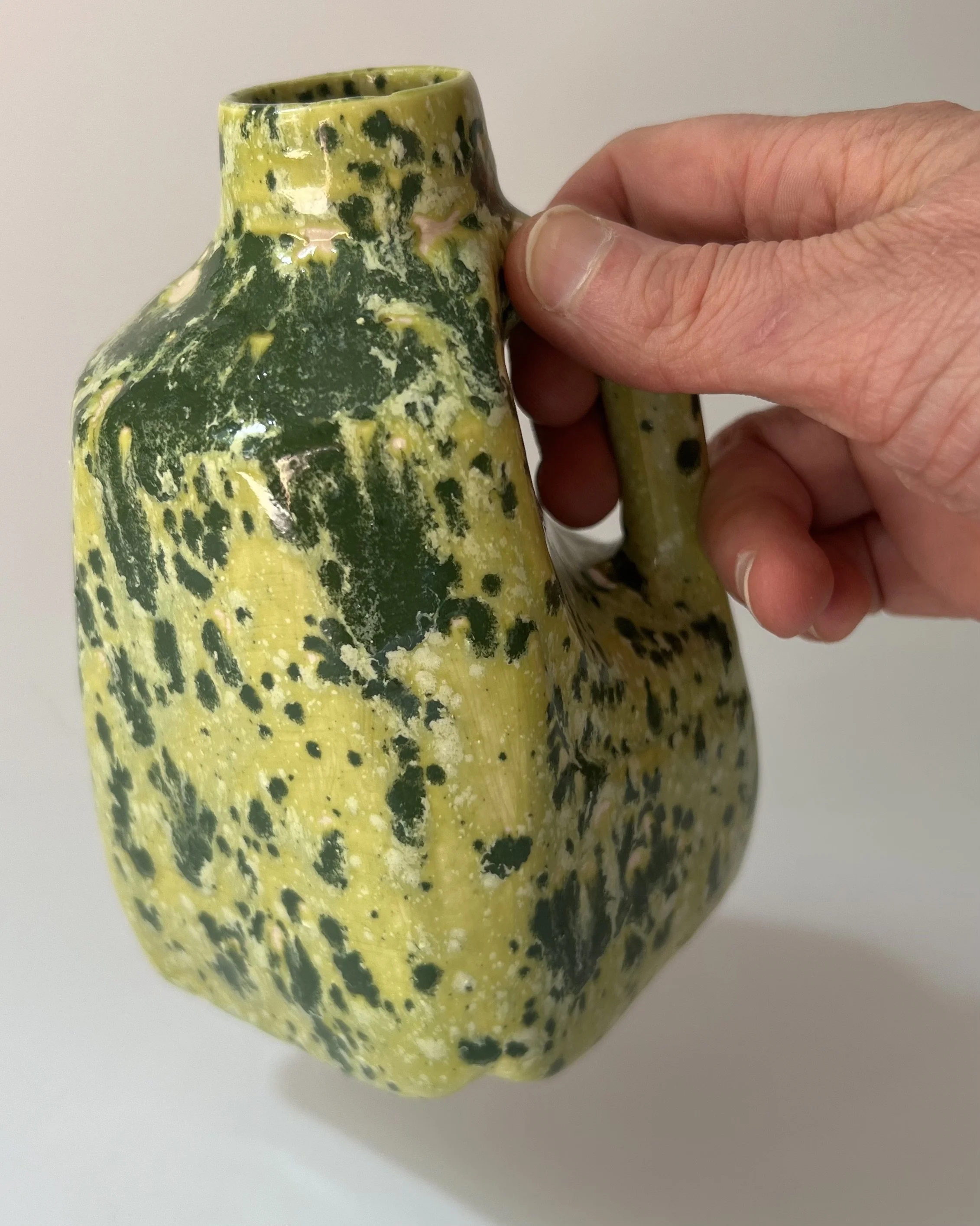 Hand holding a handmade porcelain milk jug to show its scale and sculptural form.