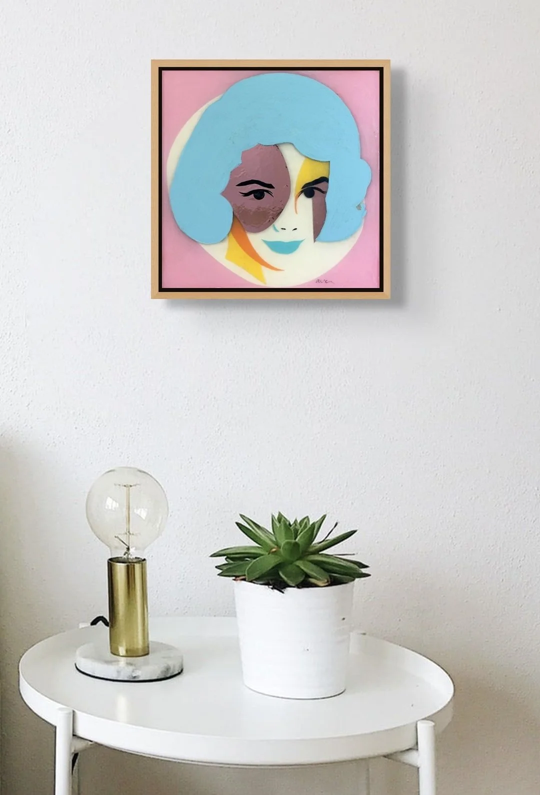 Ingrid displayed on a wall above a small table with a potted plant, illustrating the artwork's scale