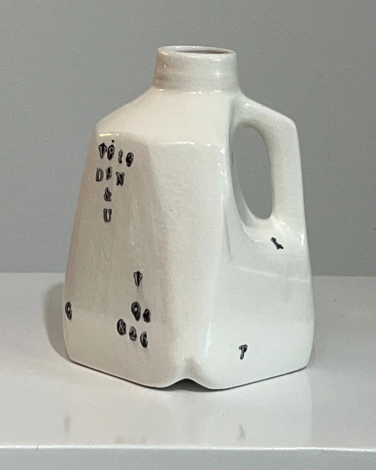Front view of a handbuilt white porcelain milk jug with scattered black typographic impressions from Alissa Van Atta's Type Series.