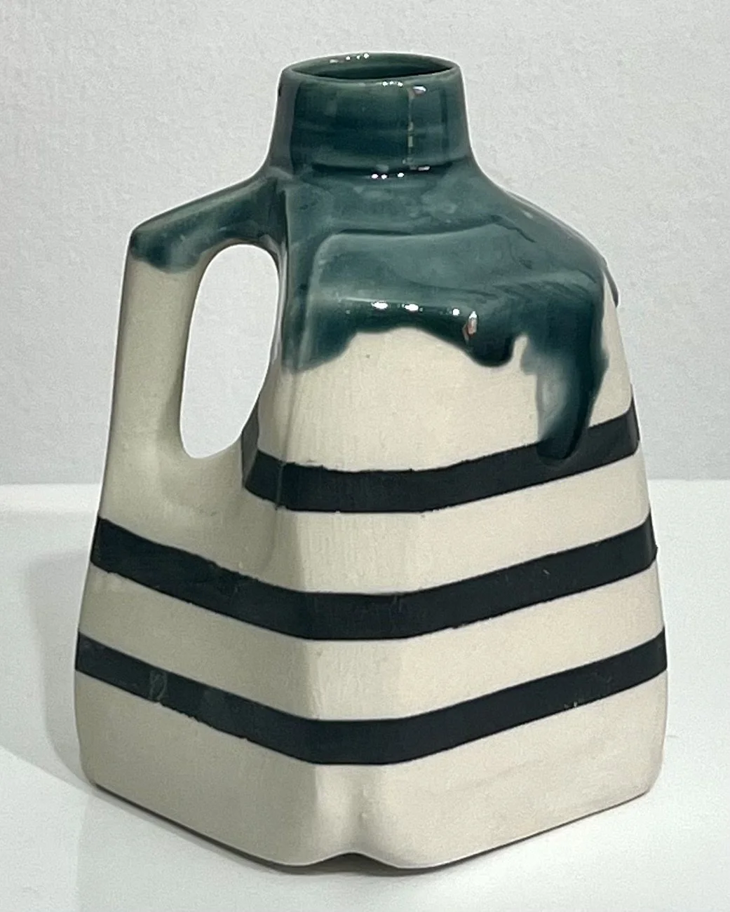 Back view of porcelain milk jug No. 26.142 by Alissa Van Atta, showing black horizontal stripes beneath glossy Rainforest green glaze.