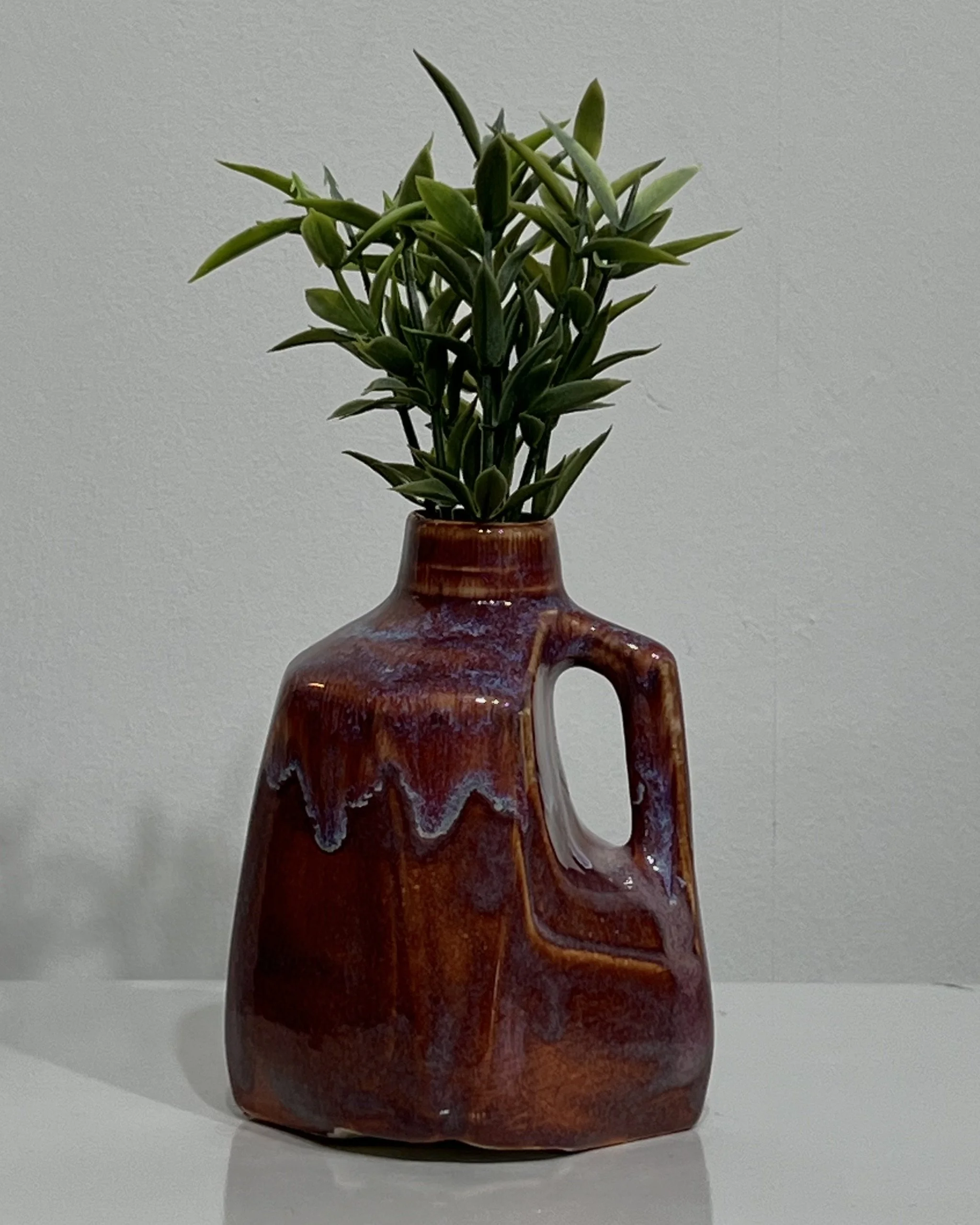 Handmade porcelain milk jug vase by Alissa Van Atta featuring deep burgundy Chun Plum and creamy Oatmeal glazes, displayed with green botanical stems.