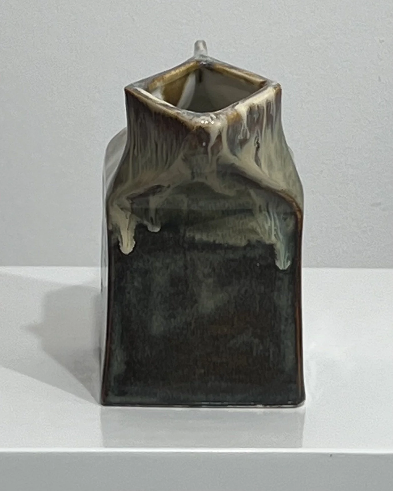 Side view of sculptural porcelain milk carton vase with layered glaze