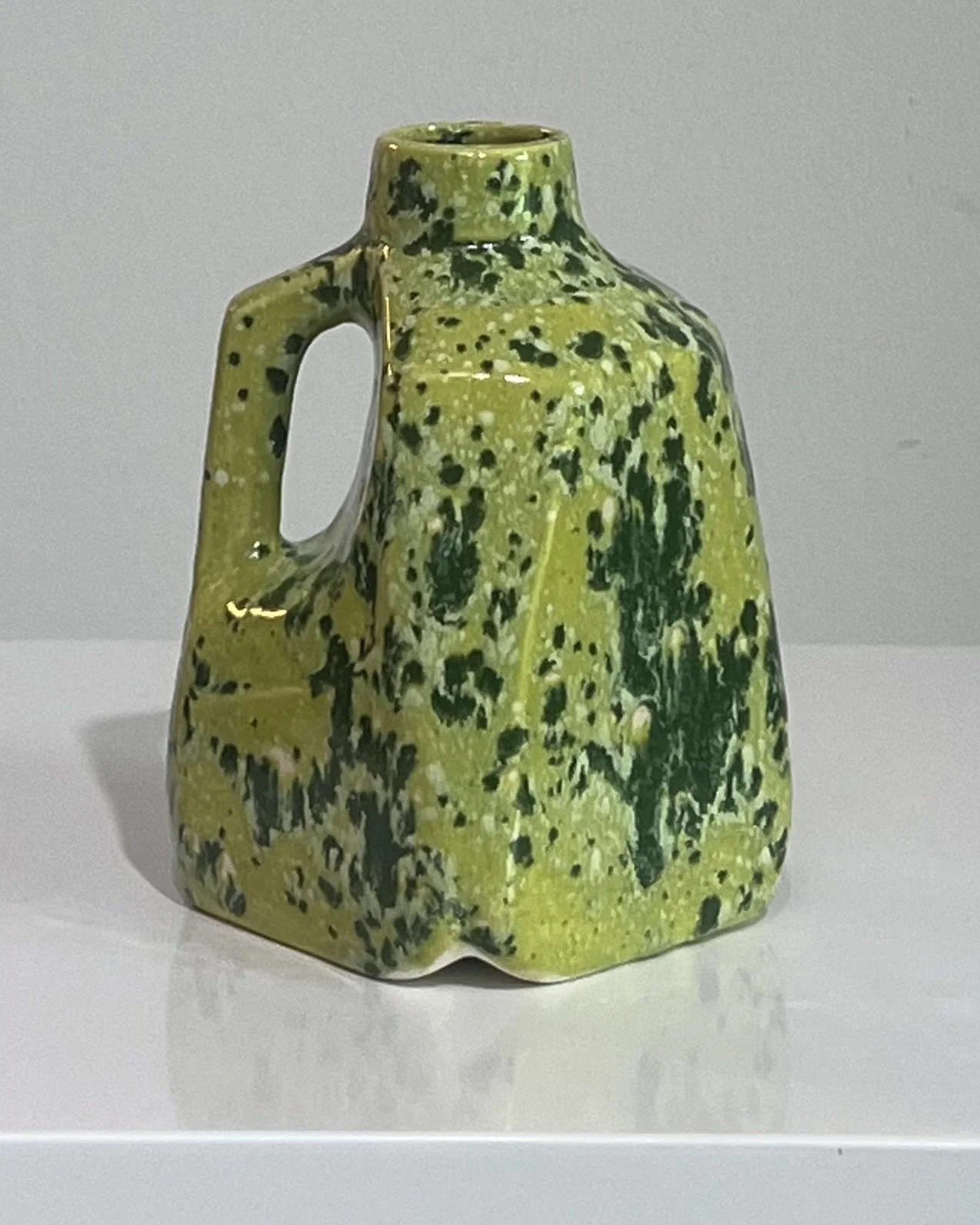 Side view of a one-of-a-kind porcelain milk jug finished in a green speckled glaze.