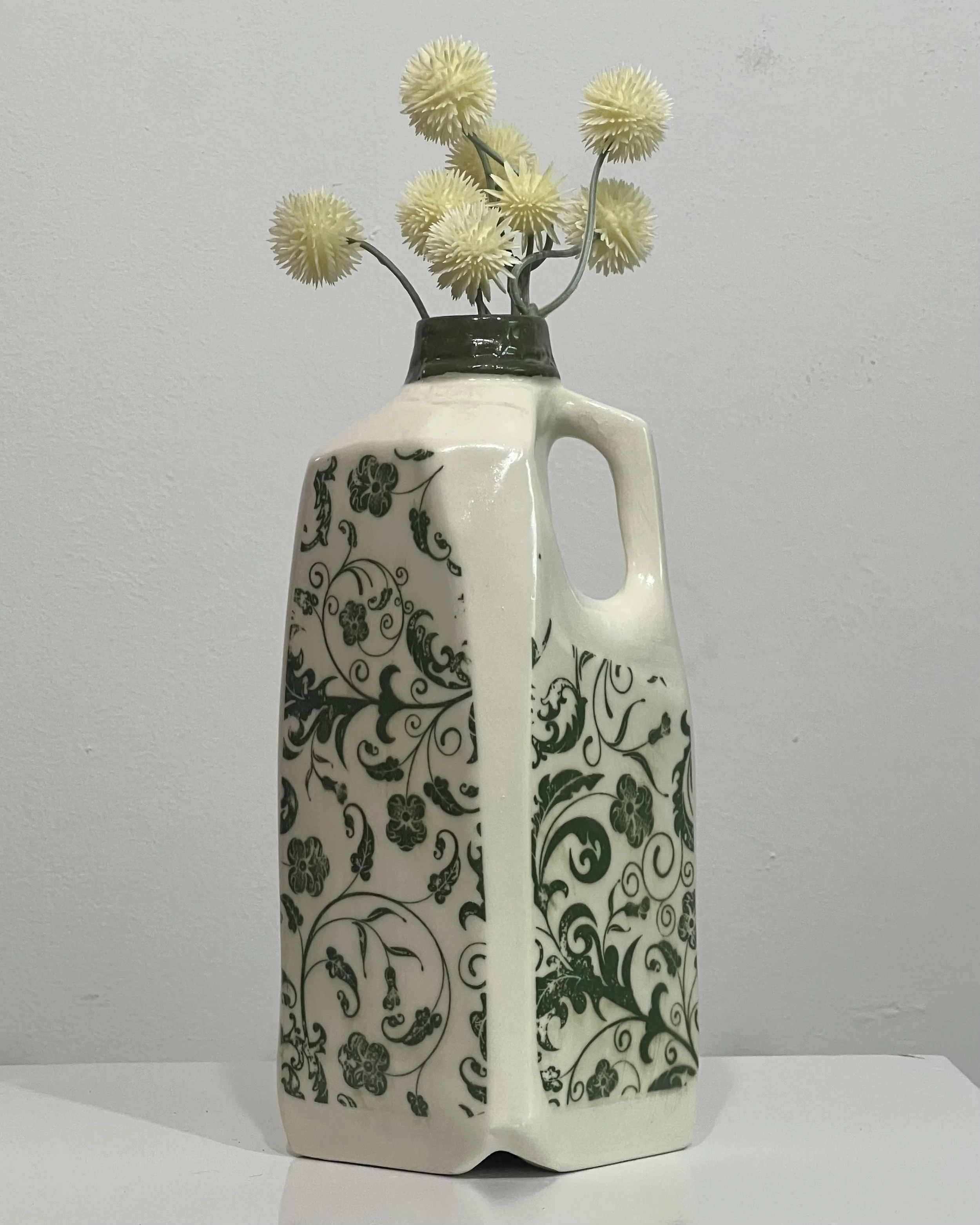 Botanical tall porcelain milk jug with green botanical transfer design holding yellow flowers.