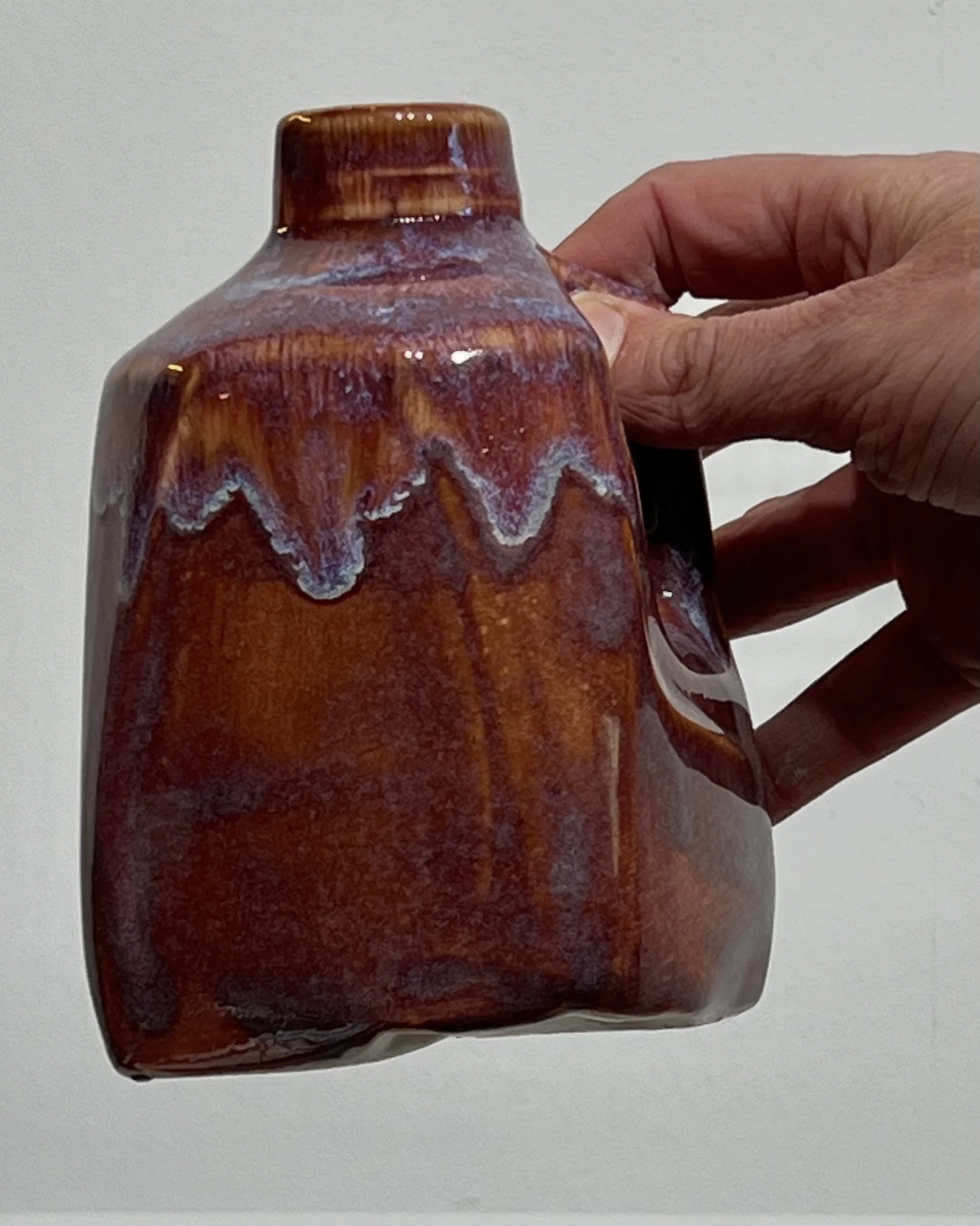Handmade burgundy porcelain milk jug held in hand to demonstrate its small size