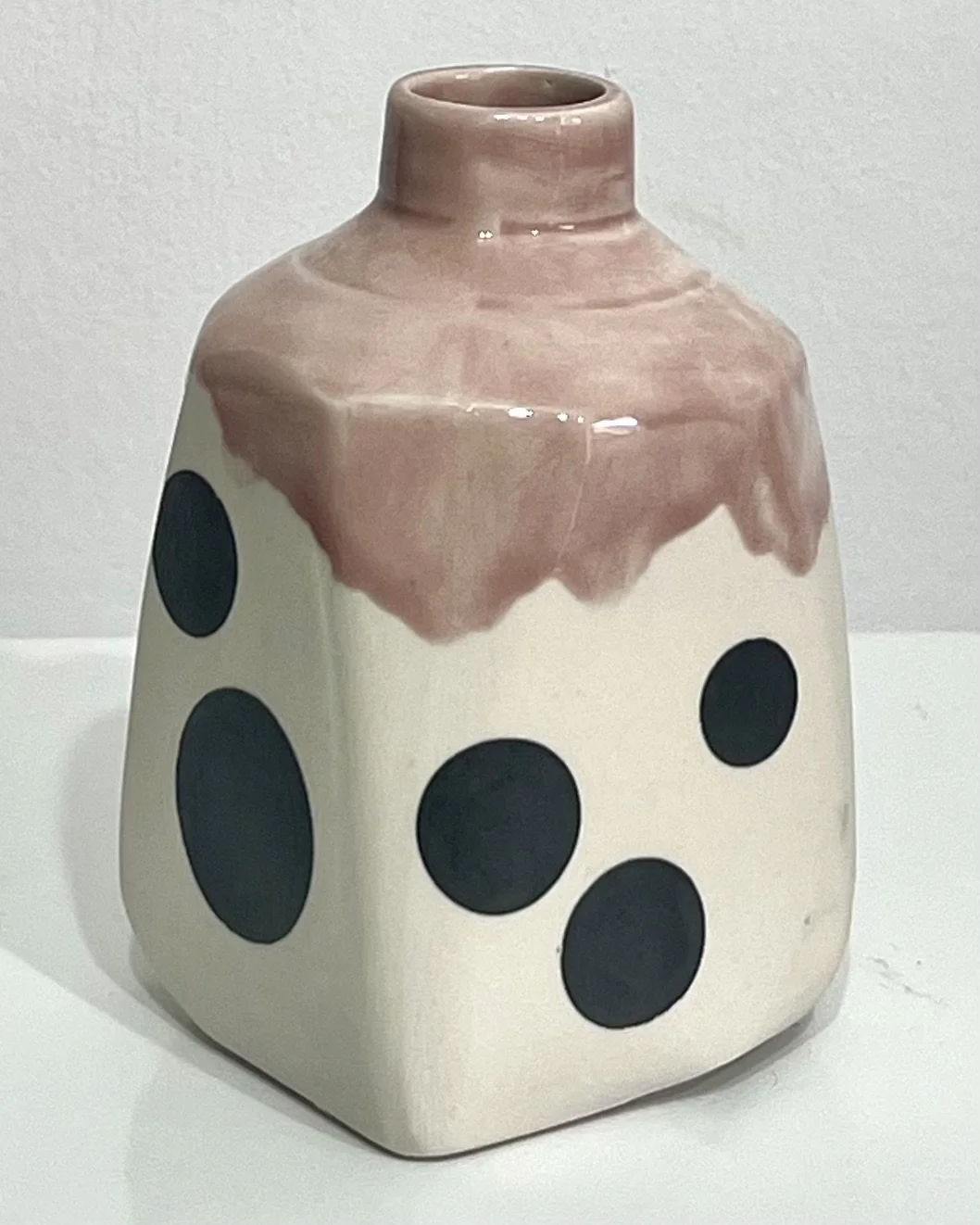 Side view of handcrafted porcelain milk jug No. 26.149, showing its small handle, scattered black dots, and warm pinkish-brown Weeping Plum glaze.