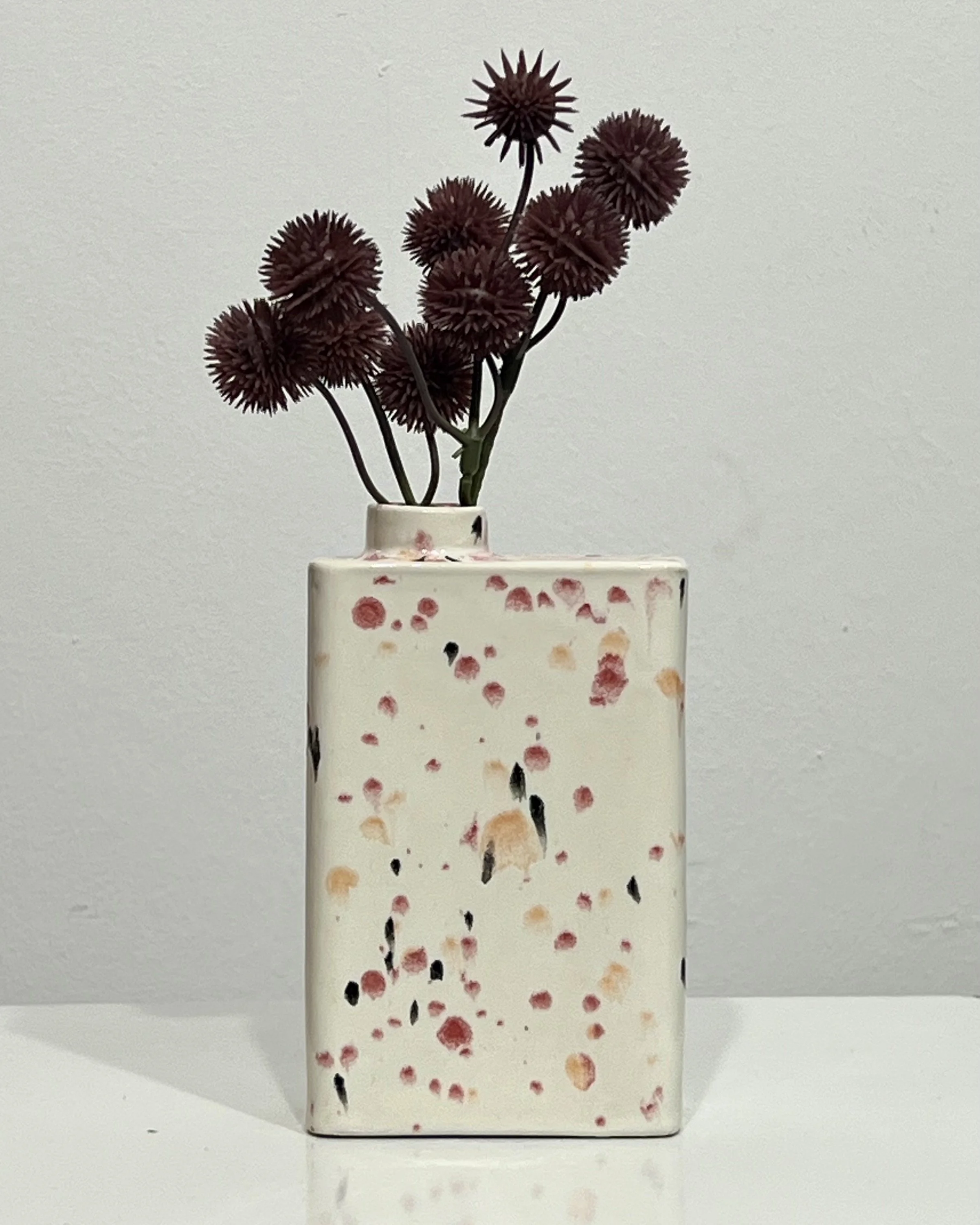 Poppy Fields porcelain carton vase C26.6 with burgundy globe thistle stems, featuring red, peach, and black speckles on a cream glaze.