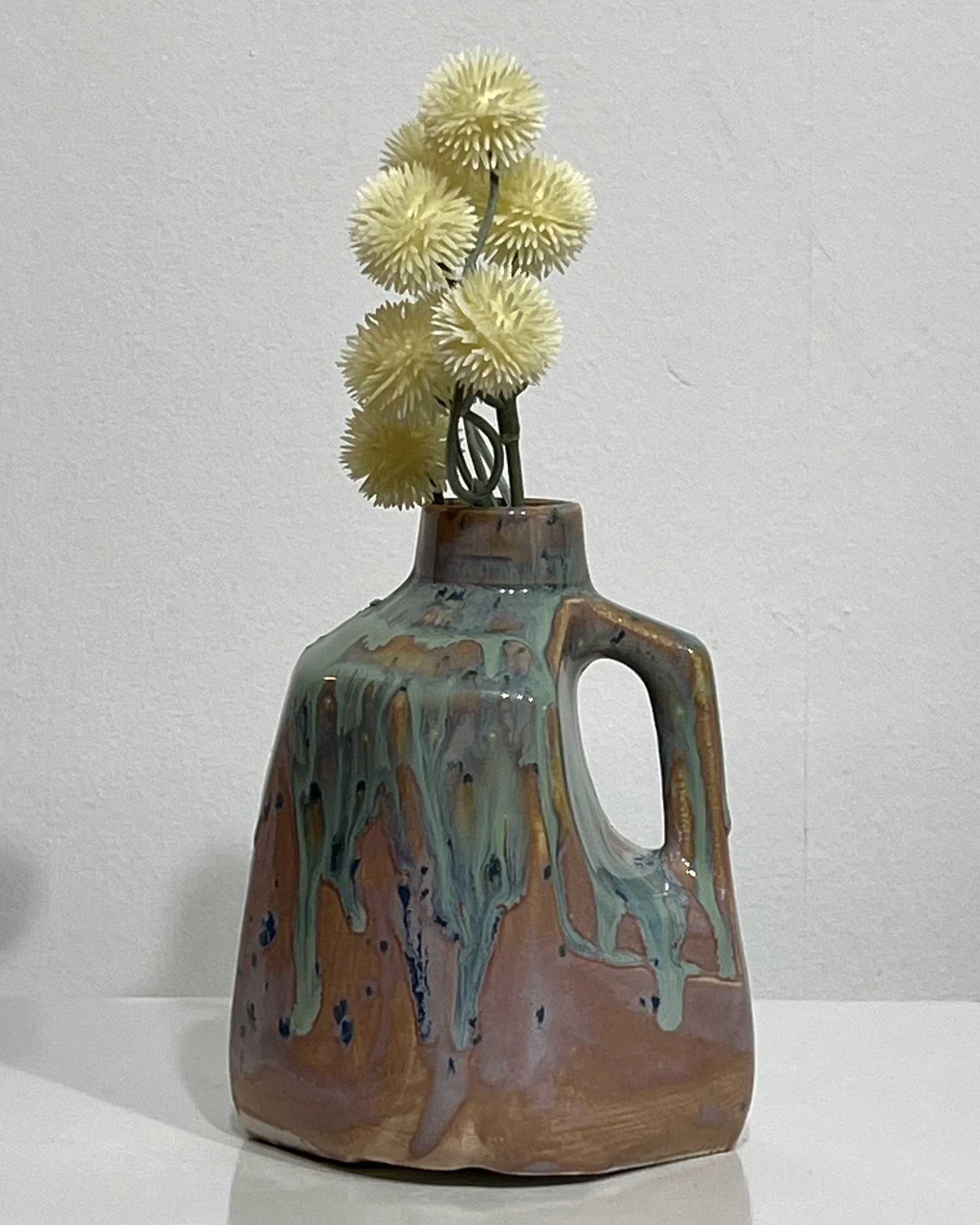 Handmade porcelain milk jug vase by Alissa Van Atta featuring Purple Aster and Micro Jade glazes in rosy pink and turquoise-green, styled with yellow flowers.