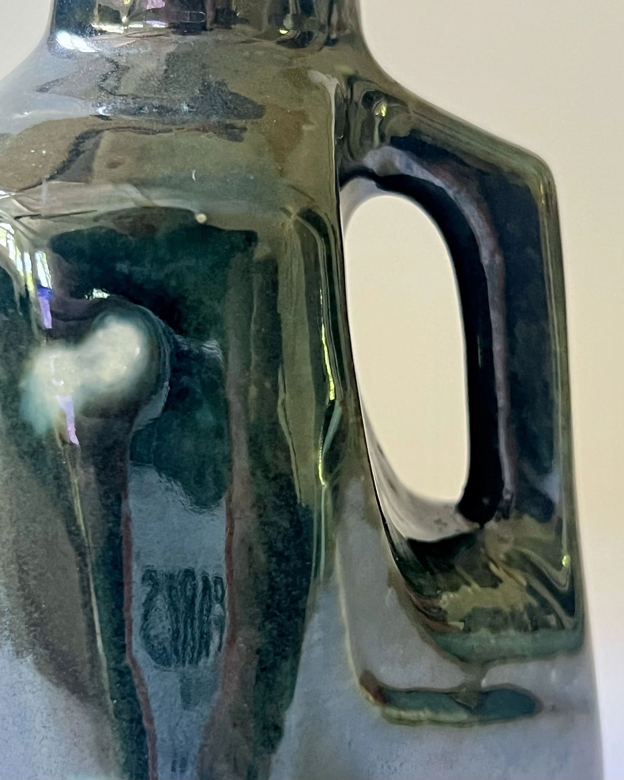 Close-up detail of porcelain milk jug vase handle with flowing Vintage Gold over Rainforest glaze.