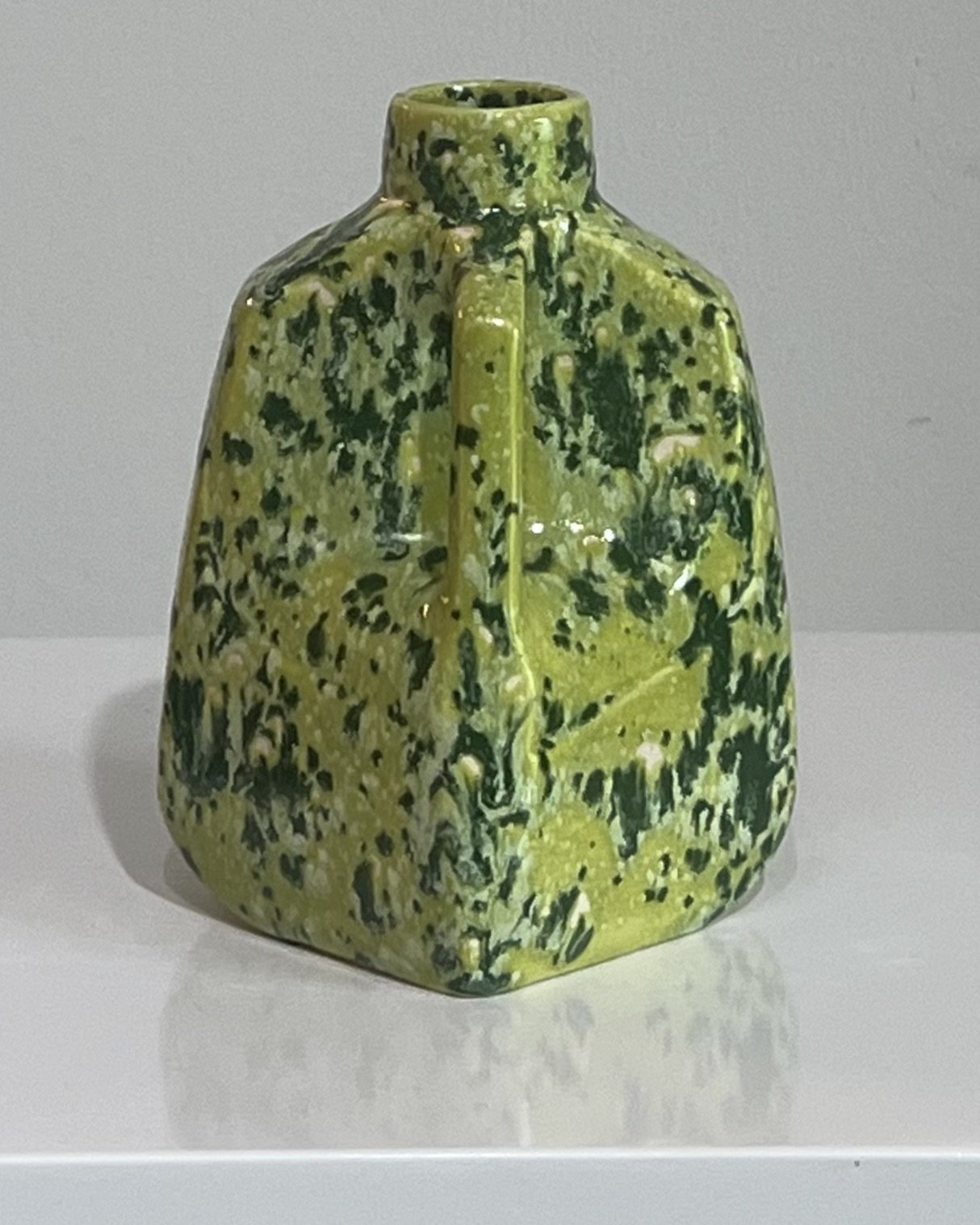 Corner view of a contemporary porcelain milk jug with a richly textured green speckled glaze.