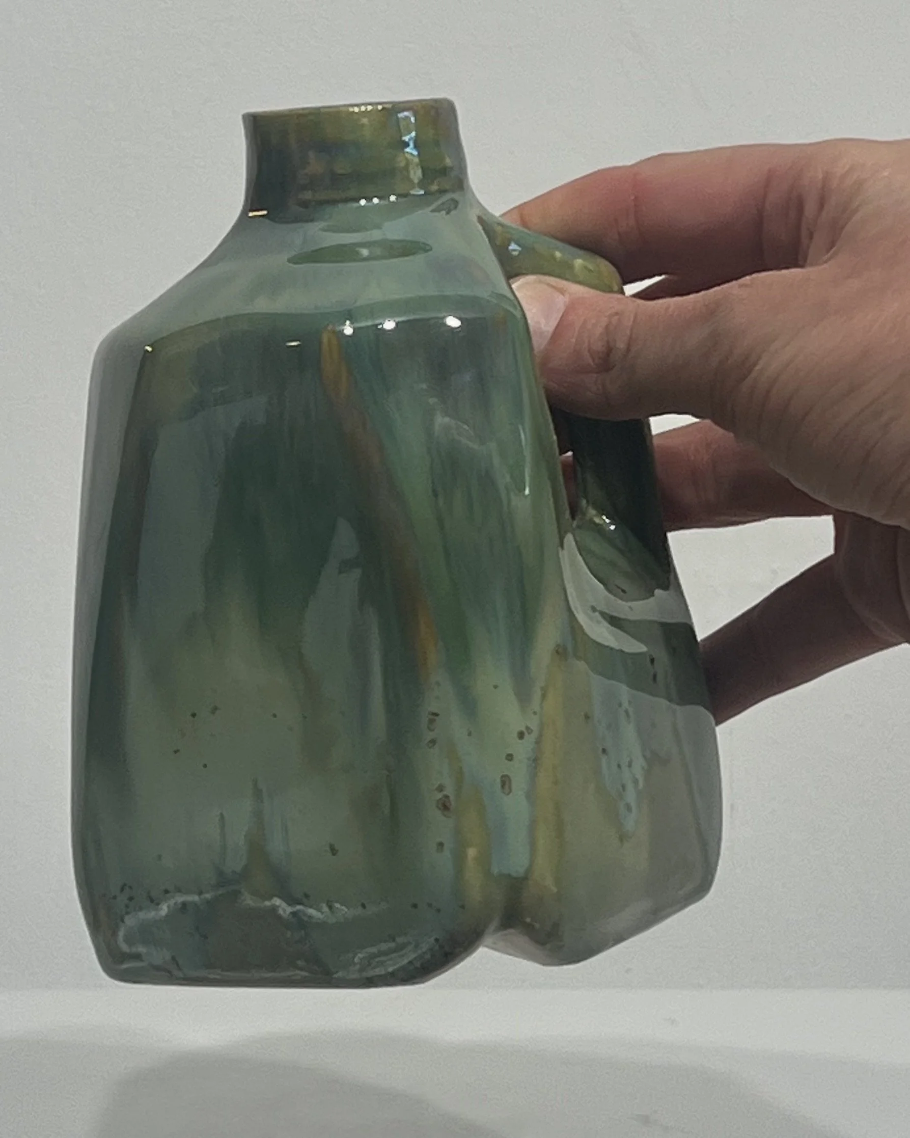 Hand holding a small handmade porcelain milk jug to demonstrate its size and proportions.
