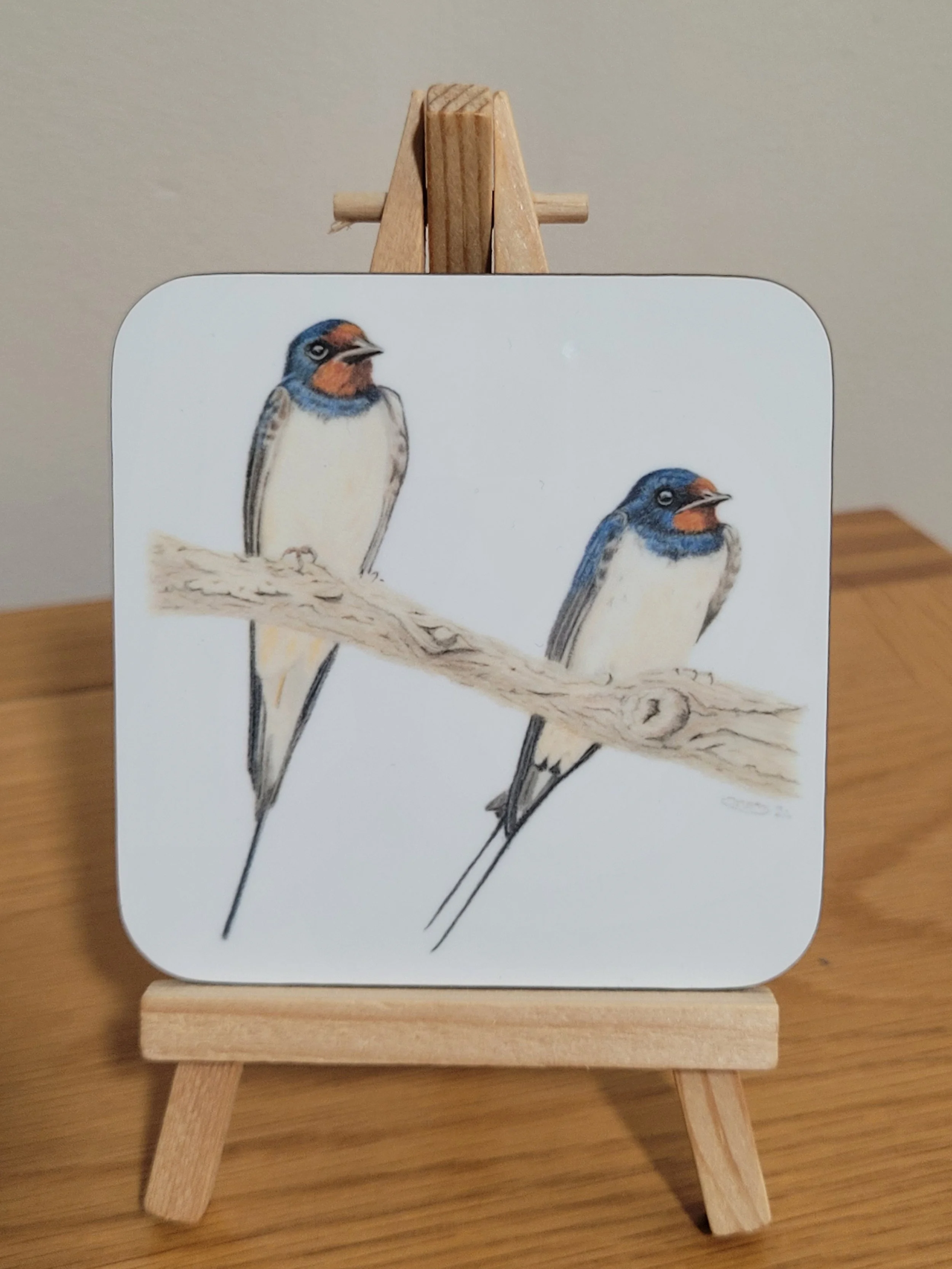 An individual glossy coaster with a pair of swallows on it.