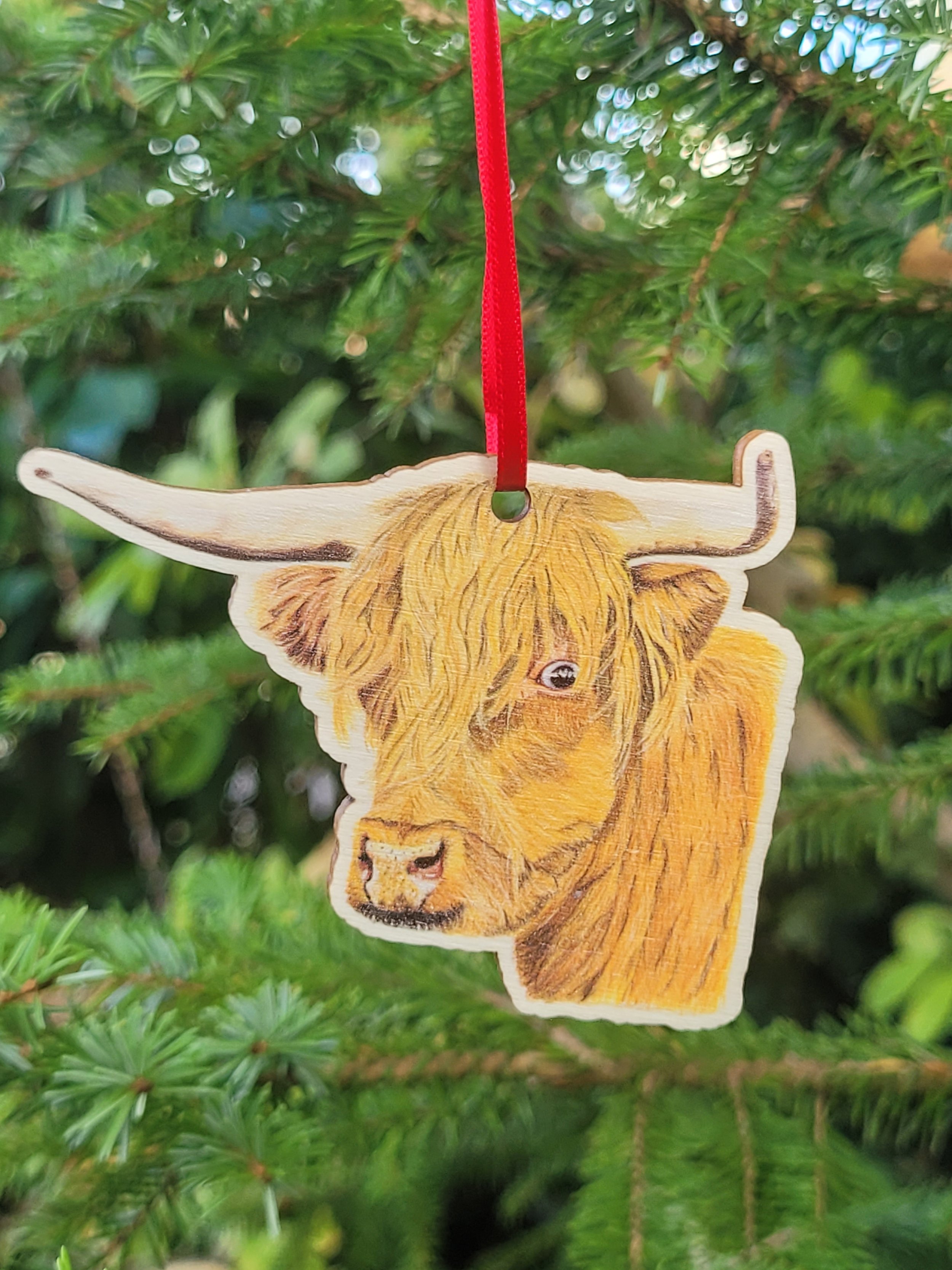 A highland cow wooden Christmas decoration with a red ribbon.