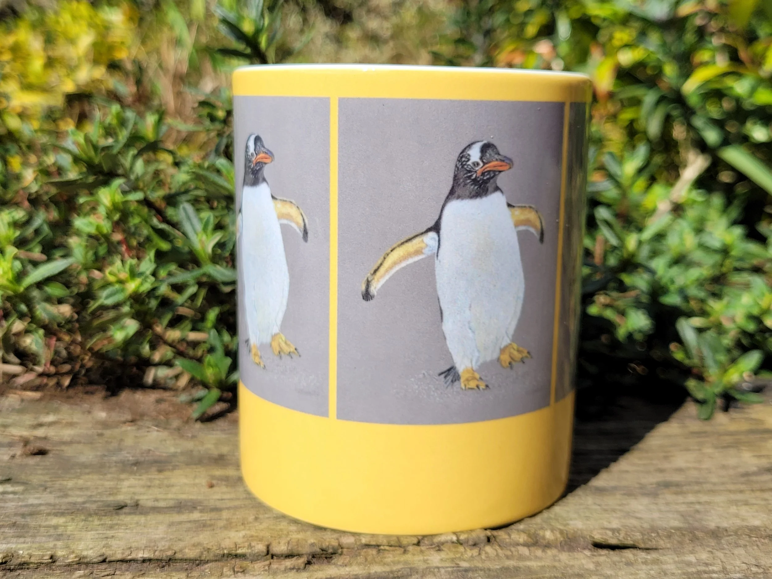 A Gentoo penguin ceramic mug with a yellow background.