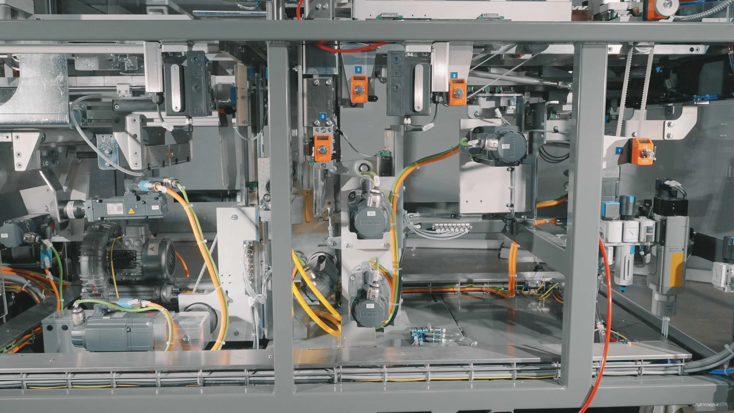 Close-up of industrial machinery with various motors, sensors, cables, and metal components arranged within a metal frame.