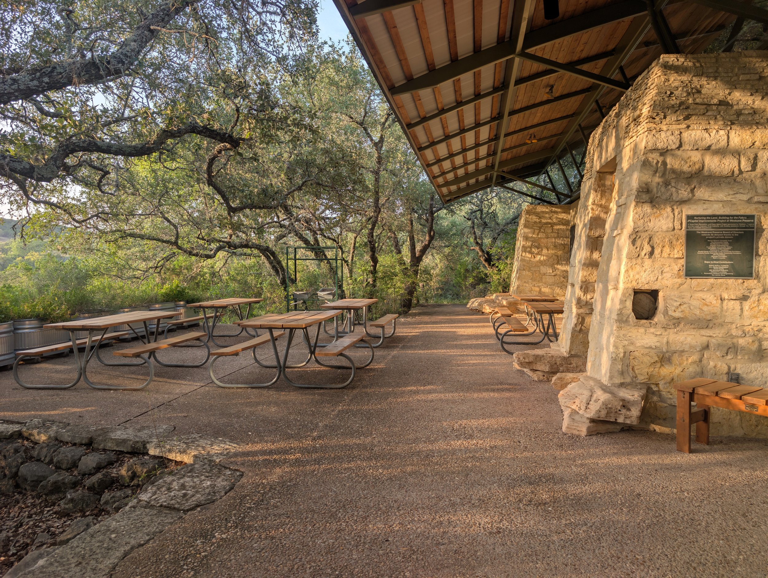 Outdoor seating area at the environmental learning center with picnic tables near a stone structure and large trees with twisted branches.