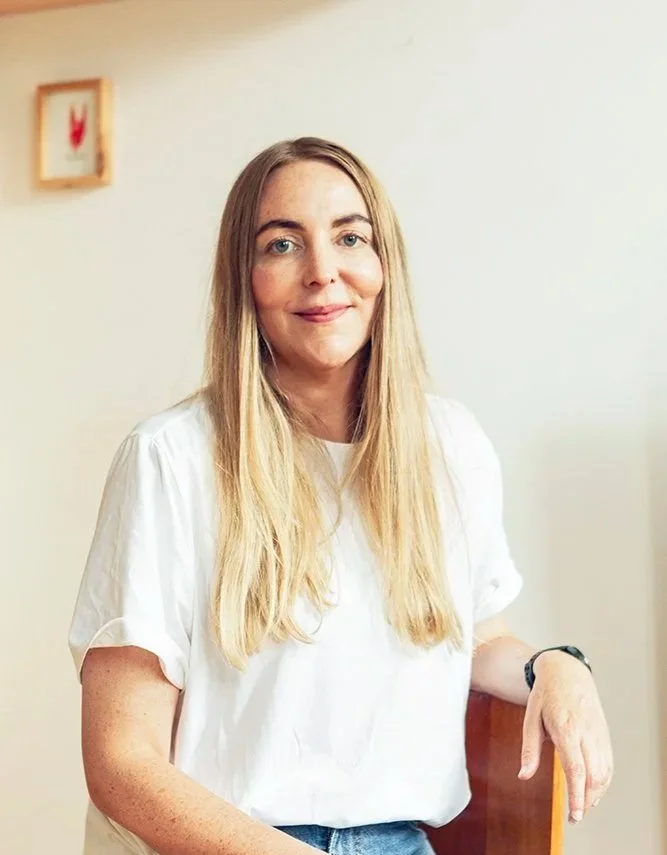En kvinde med langt blondt hår, iført hvid T-shirt med hvid væg.