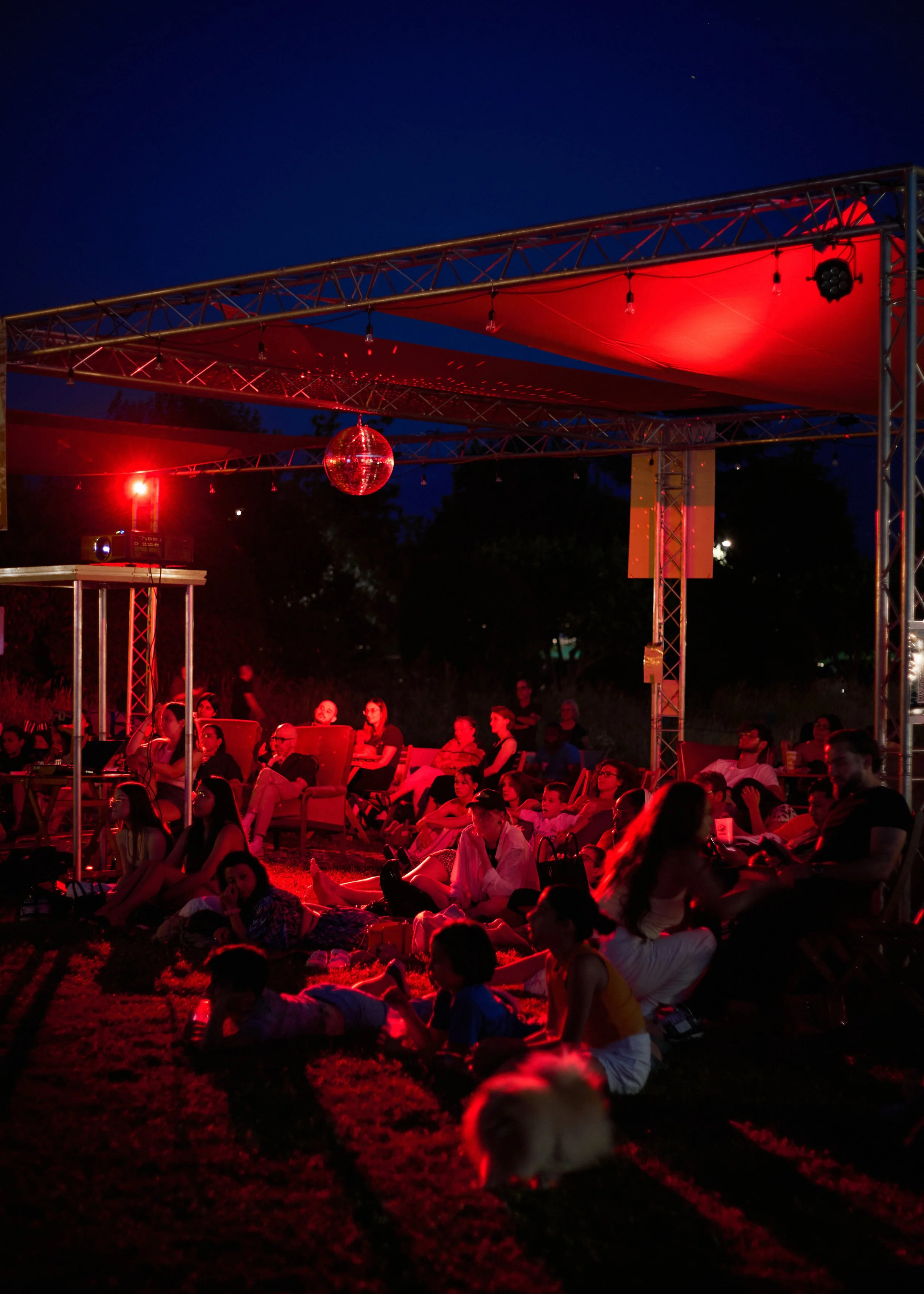 Groupe de personnes assises sous une tente rouge lors d'une soirée, avec une boule disco suspendue, en plein air la nuit.