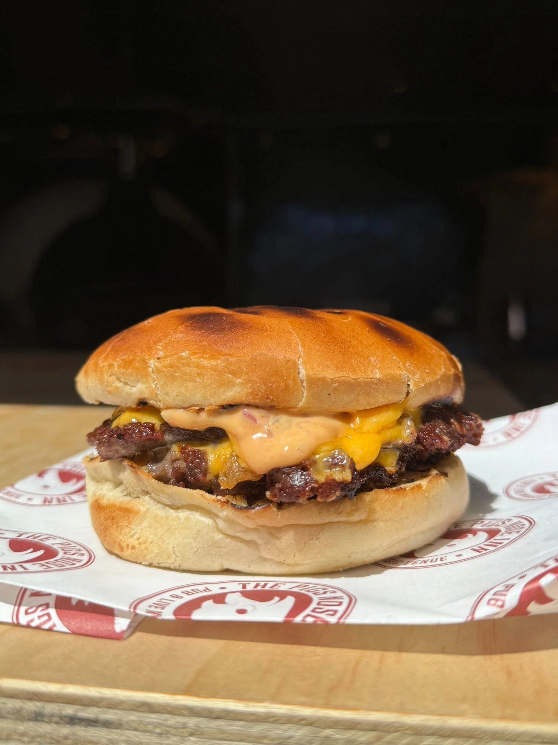 Close-up of a cheeseburger with beef patty, melted cheese, and sauce in a bun on a paper wrapper, on a wooden surface.