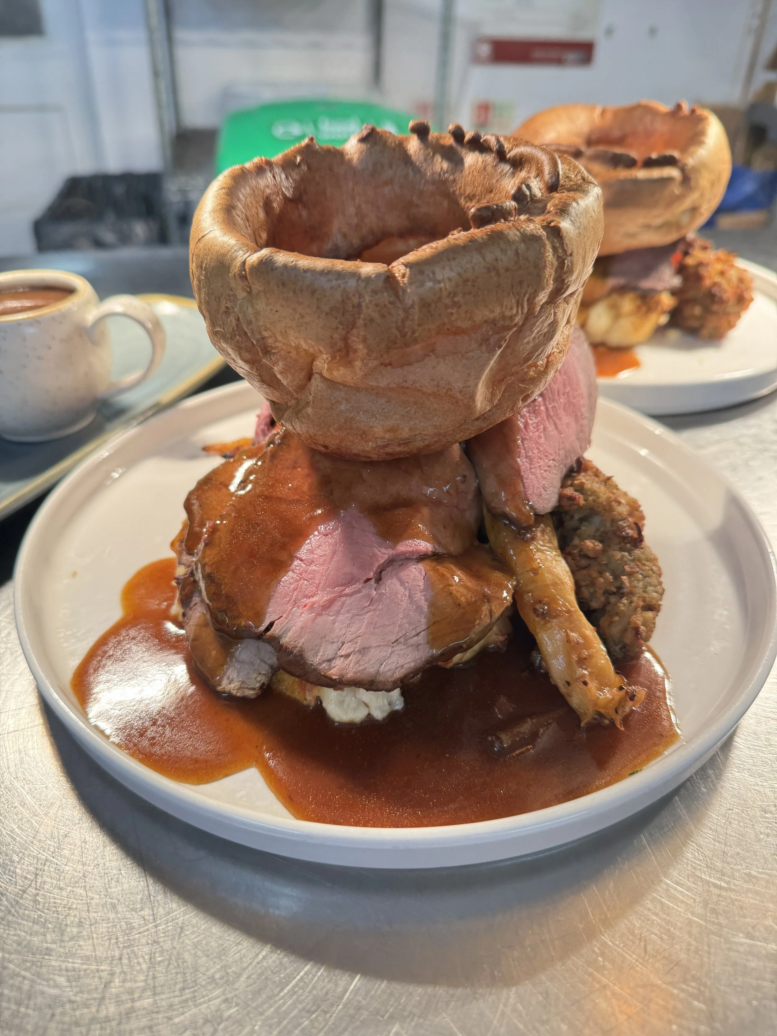 A plate of food featuring a large Yorkshire pudding, slices of roast beef with gravy, a roast chicken leg, and various sides with brown gravy.