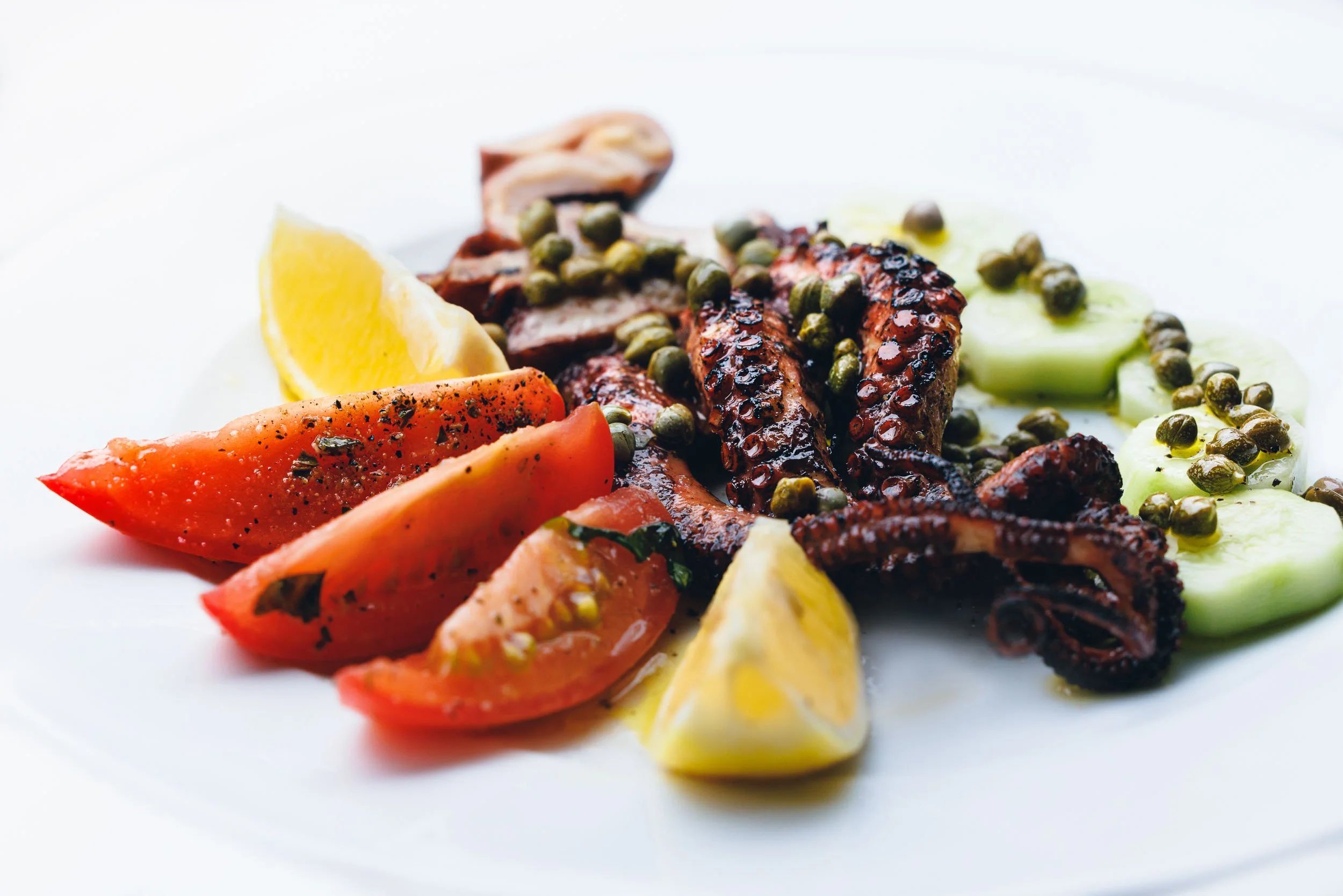 Gourmet grilled octopus plating, professional Mediterranean seafood photography, charred octopus with lemon and tomatoes editorial, high-end restaurant menu imagery, vibrant culinary food styling.