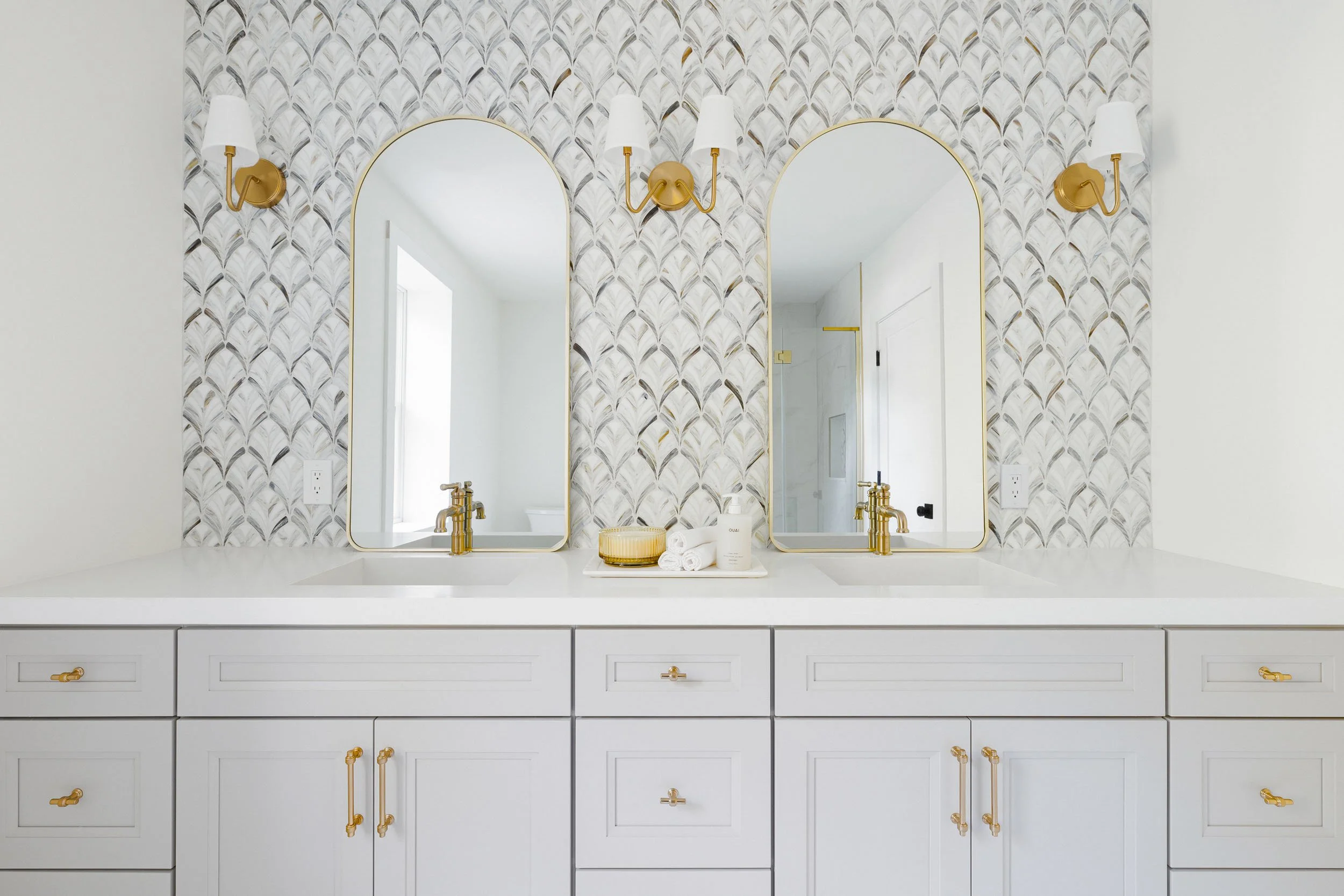 Luxury residential bathroom photography, double sink marble vanity with gold fixtures and arched mirrors, interior designer showcase featuring decorative scallop tile backsplash, symmetrical primary bath design by professional interior decorator, hig