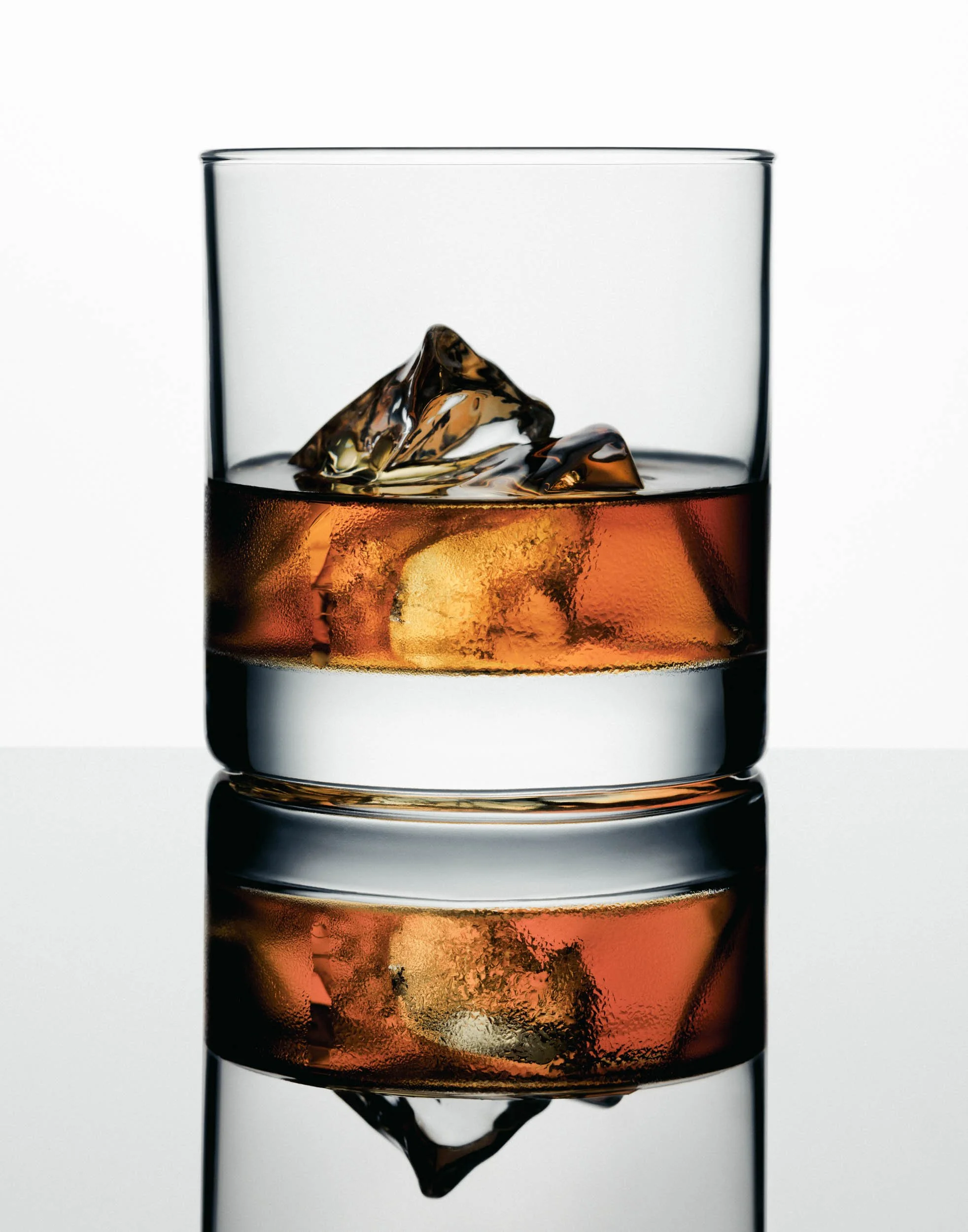 NYC beverage product photography by Jeff Rainone featuring whiskey on ice in a rocks glass with reflection, premium spirits commercial imagery.