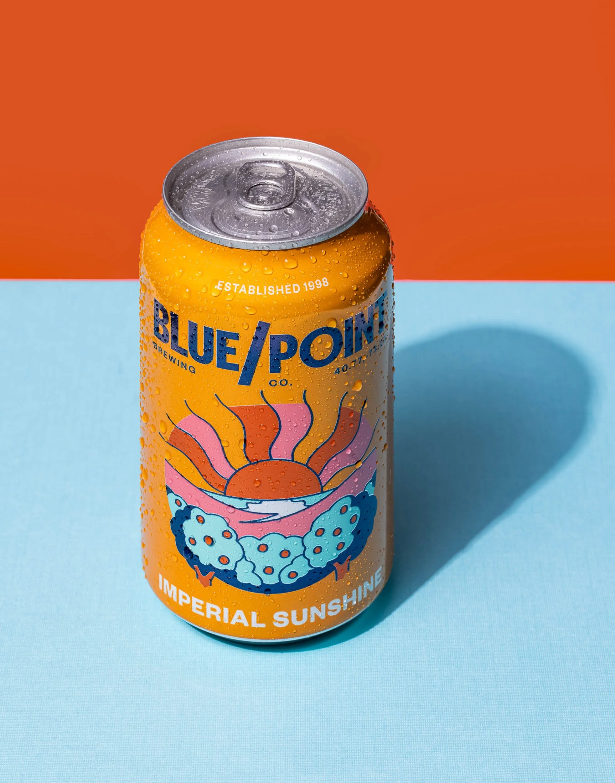 Blue Point Imperial Sunshine Blonde Ale product photography, orange and blue color block beverage branding, professional craft beer can styling, vibrant summer drink advertising, citrus ale commercial hero shot.