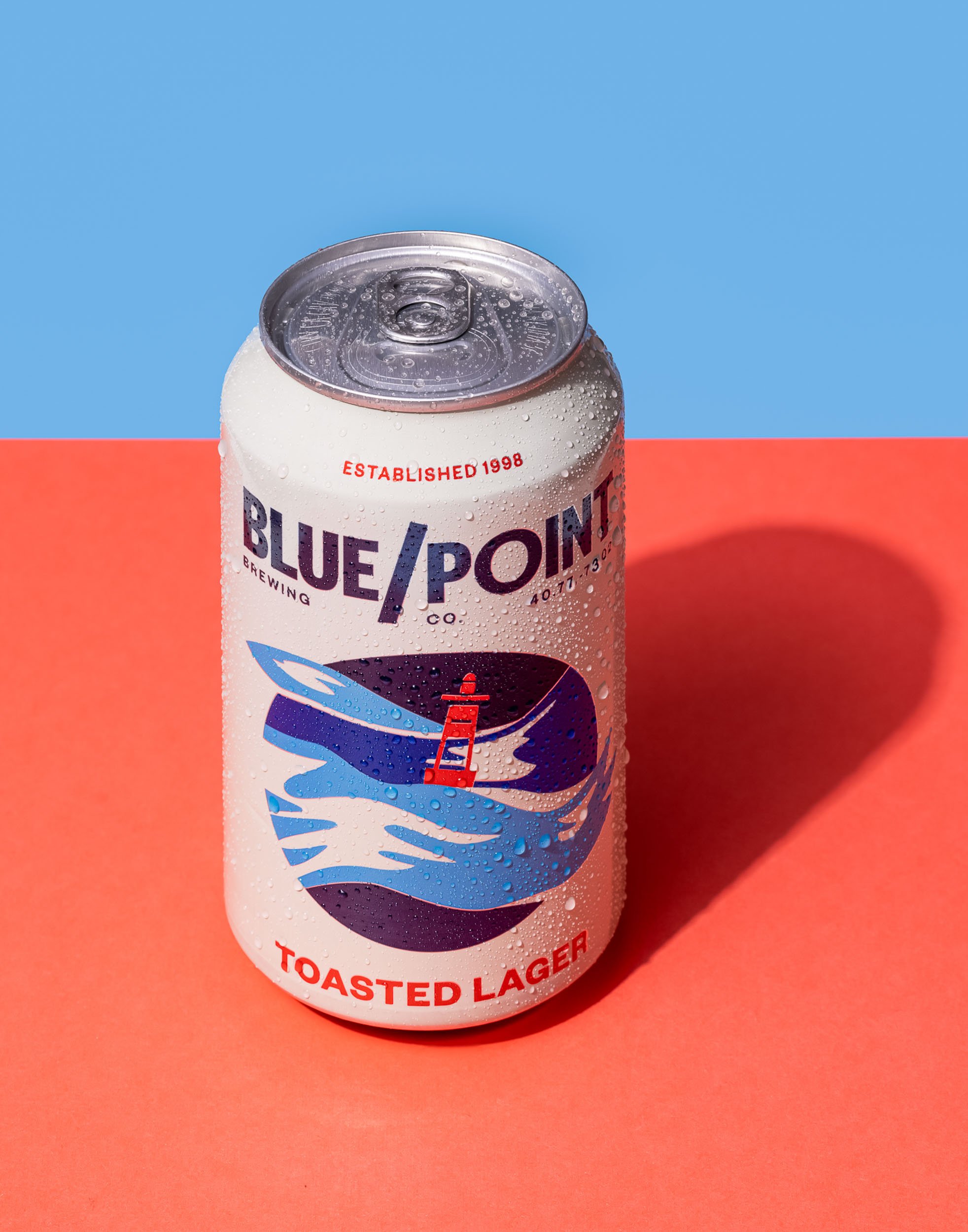 Blue Point Toasted Lager beer can photography, blue and red minimalist beverage branding, classic American lager product shot, clean commercial brewery catalog imagery, professional beer can lighting and texture.