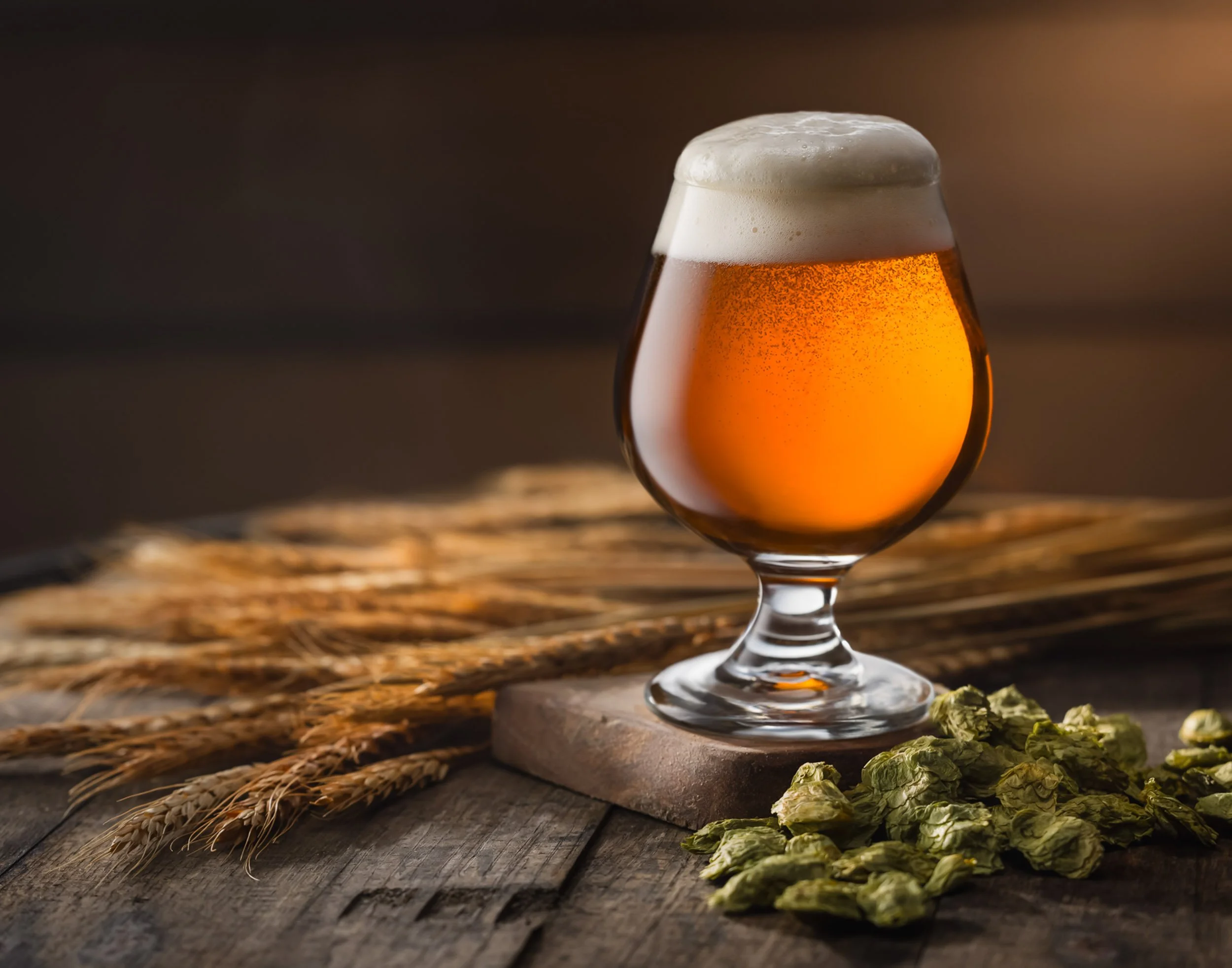 Professional wheat beer photography on rustic wooden barrel, craft beer hero shot with perfect foam head, brewery branding with raw hops and wheat stalks, farm-to-glass culinary imagery, technical lighting for hazy golden ale and grain textures.