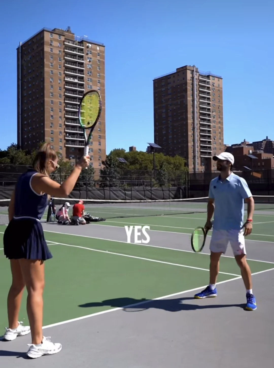 Indoor tennis court with a green curtain wall, net in the middle, and reflective polished floor showing the curtain and ceiling.