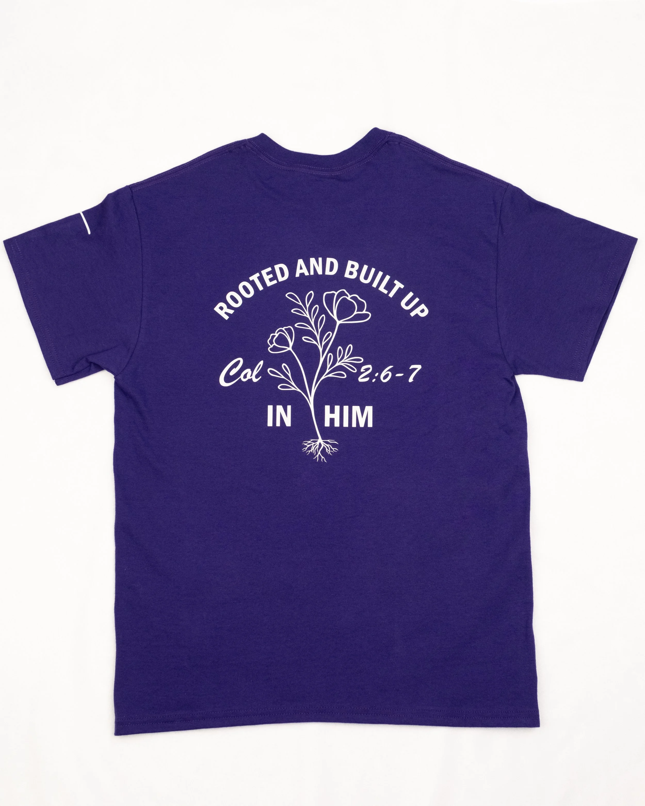 Purple t-shirt with a white floral design and the text Rooted and Built Up in Him, Colossians 2:6-7.