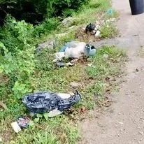 Trash and debris on the side of a dirt path with greenery in the background.