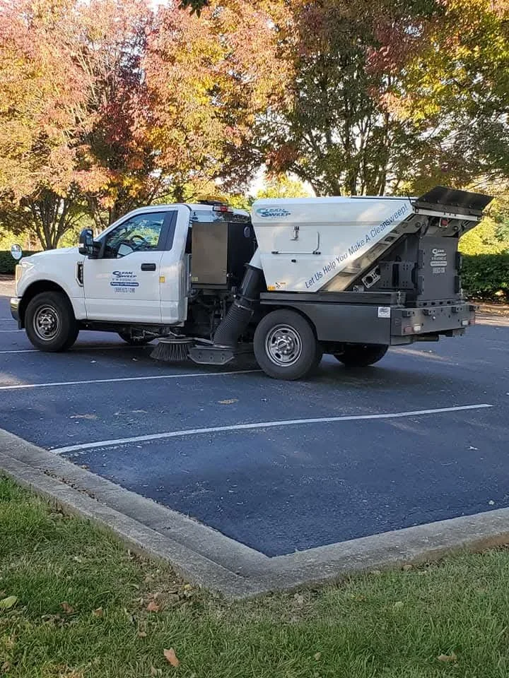 A street cleaning vehicle parked in a lot with trees in the background.