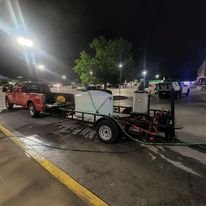 A flatbed truck parked in a parking lot at night, with equipment or generators loaded on it, illuminated by nearby streetlights.
